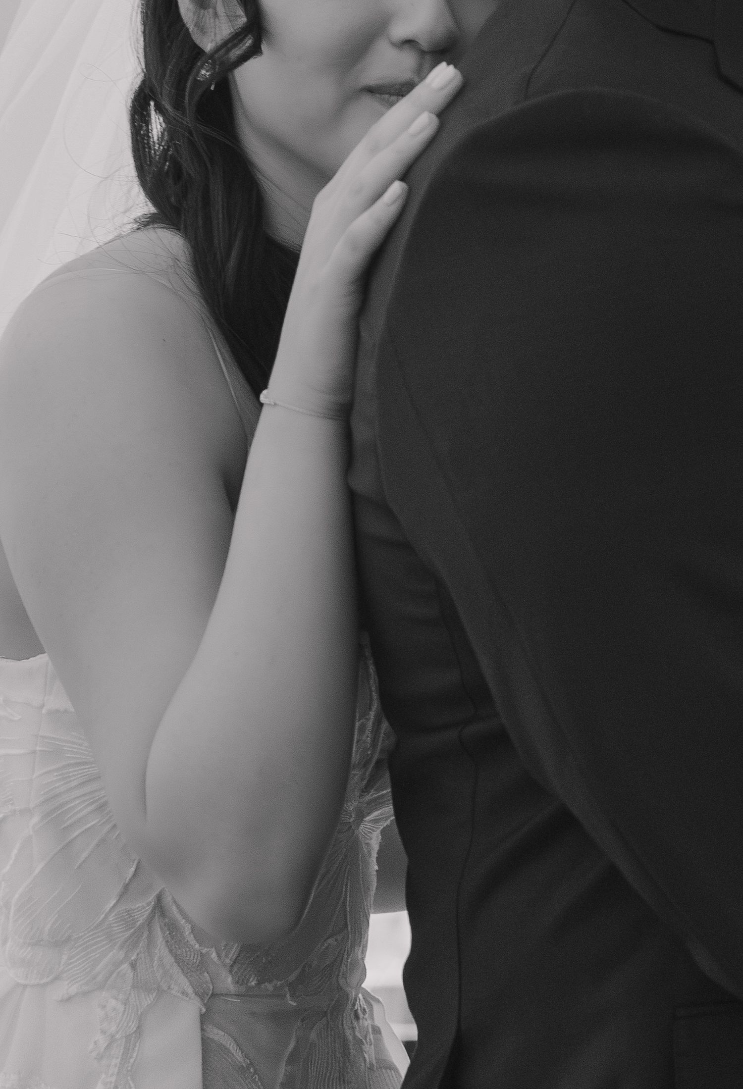 Black and white wedding photo of bride in lace gown touching groom's suit jacket in romantic close-up.