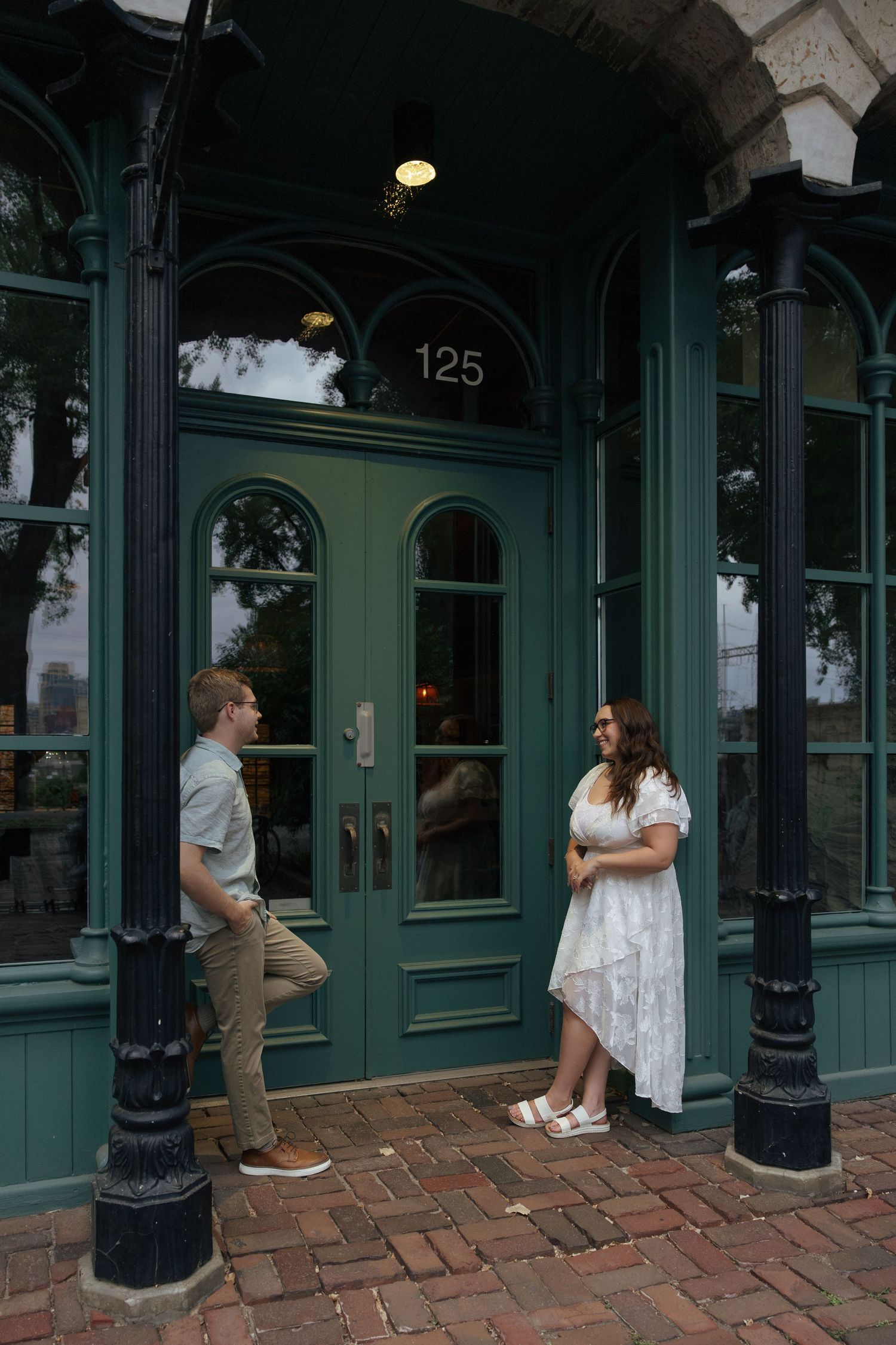 Couple standing outside a green storefront at 125, woman in white dress smiling.