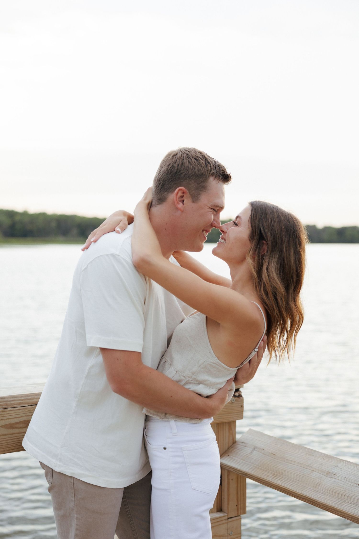 Happy couple sharing a romantic moment on a lakeside dock, embracing and laughing together.