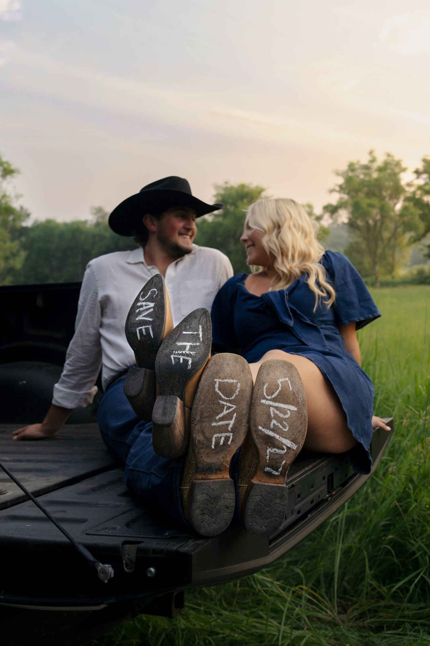 Couple sitting in truck bed with save the date written on boot soles, rustic country engagement photo.