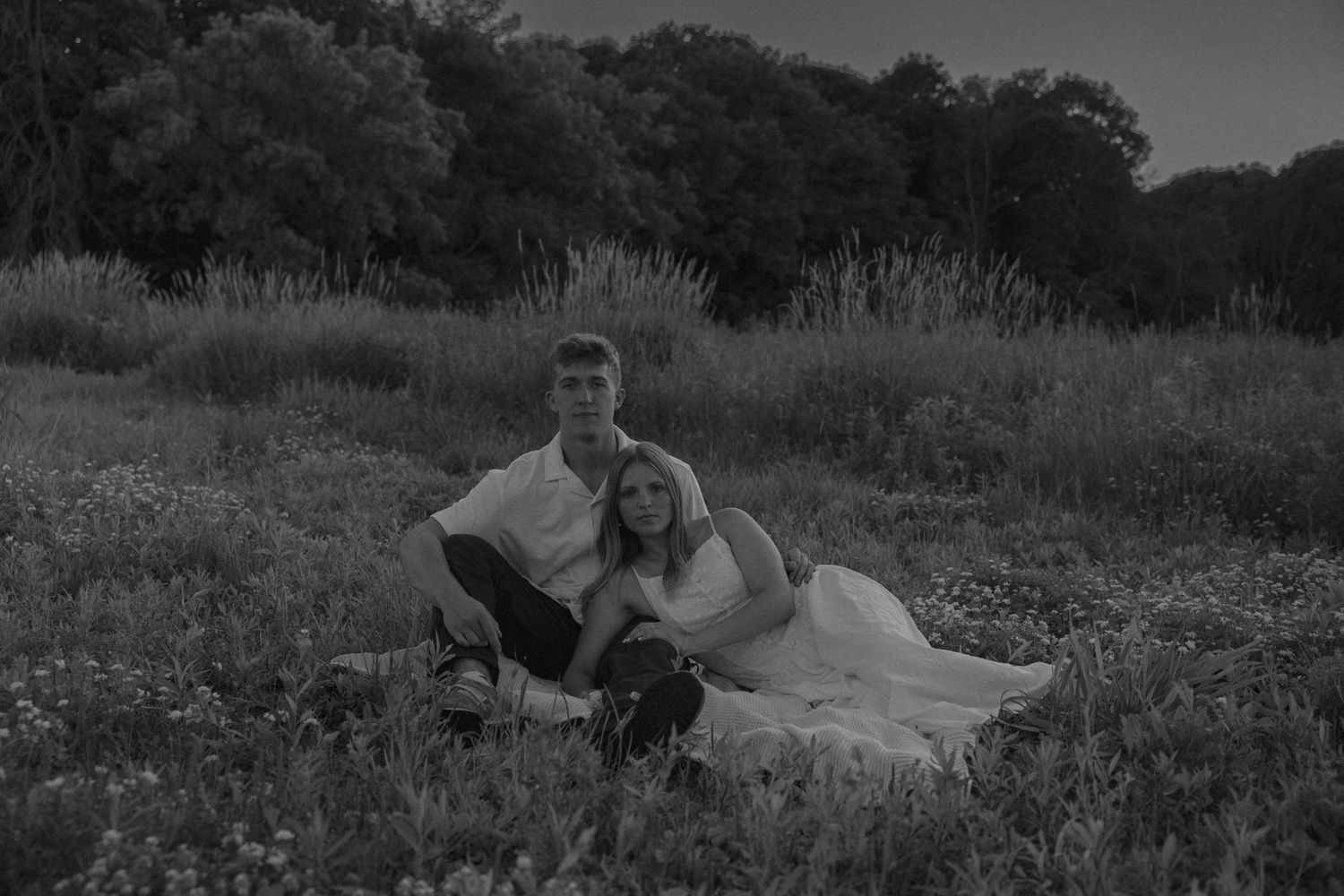 Black and white photo of a couple sitting together in a wildflower meadow at dusk.