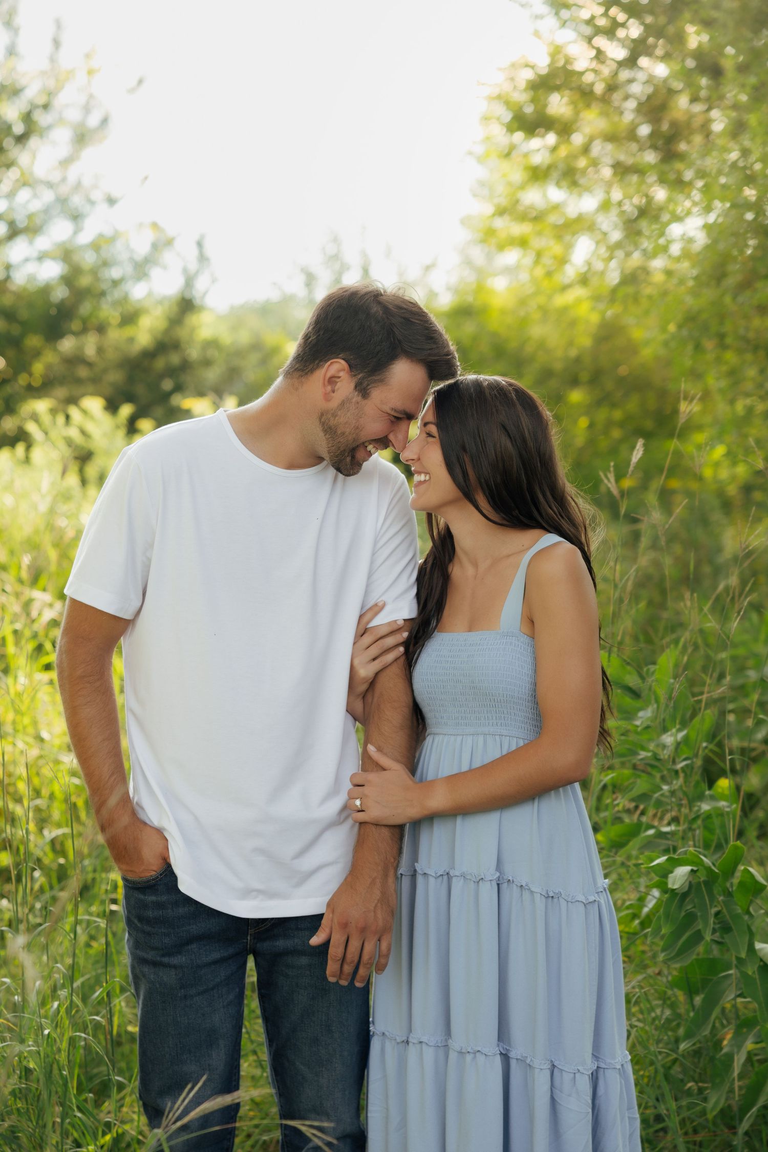 Couple sharing a romantic moment in a lush green field, man in white tee and woman in light blue sundress.