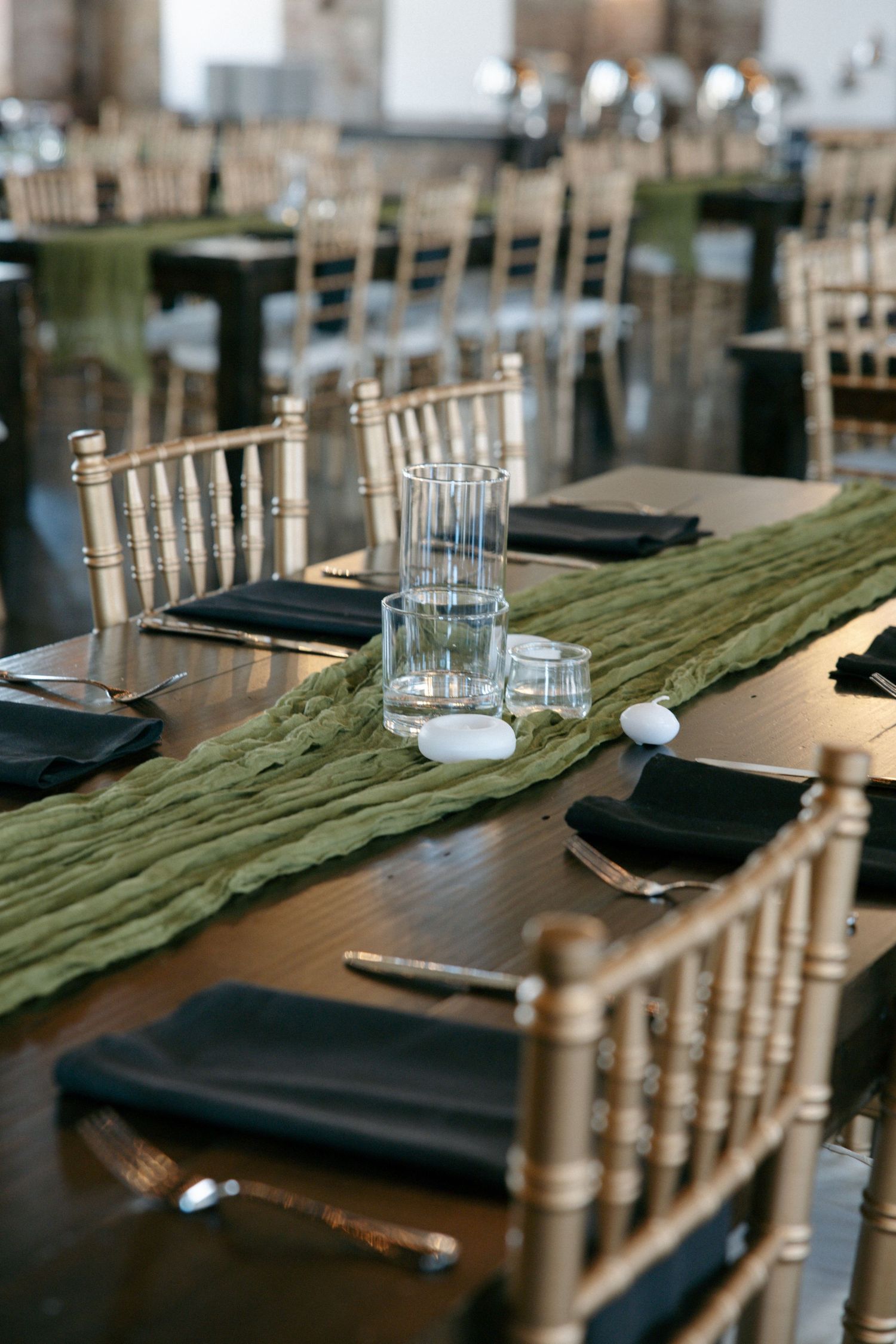 Elegant wedding reception tables with green runners, black napkins, and gold chiavari chairs.
