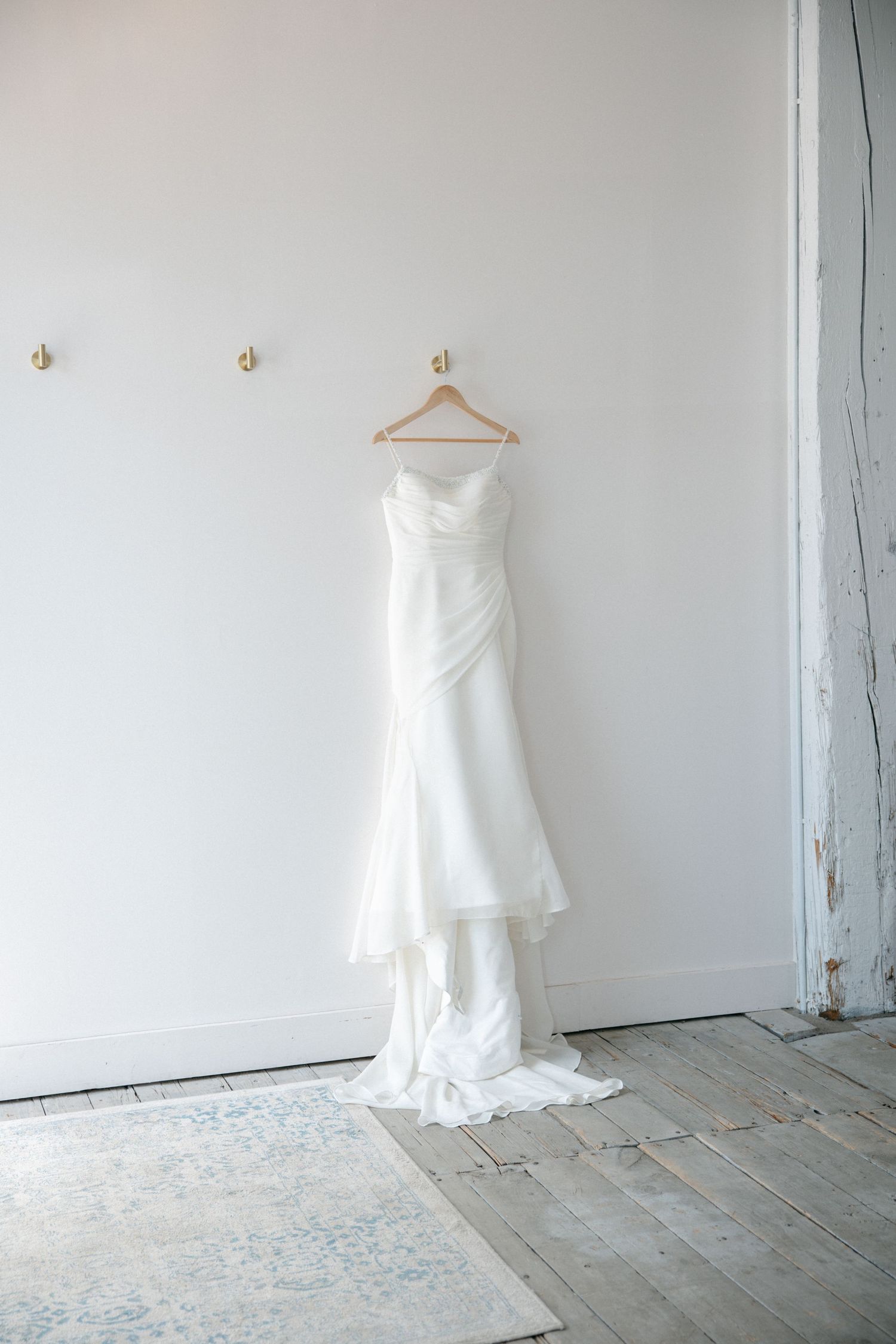 Elegant white wedding dress with a train hanging on a wooden hanger against a white wall.
