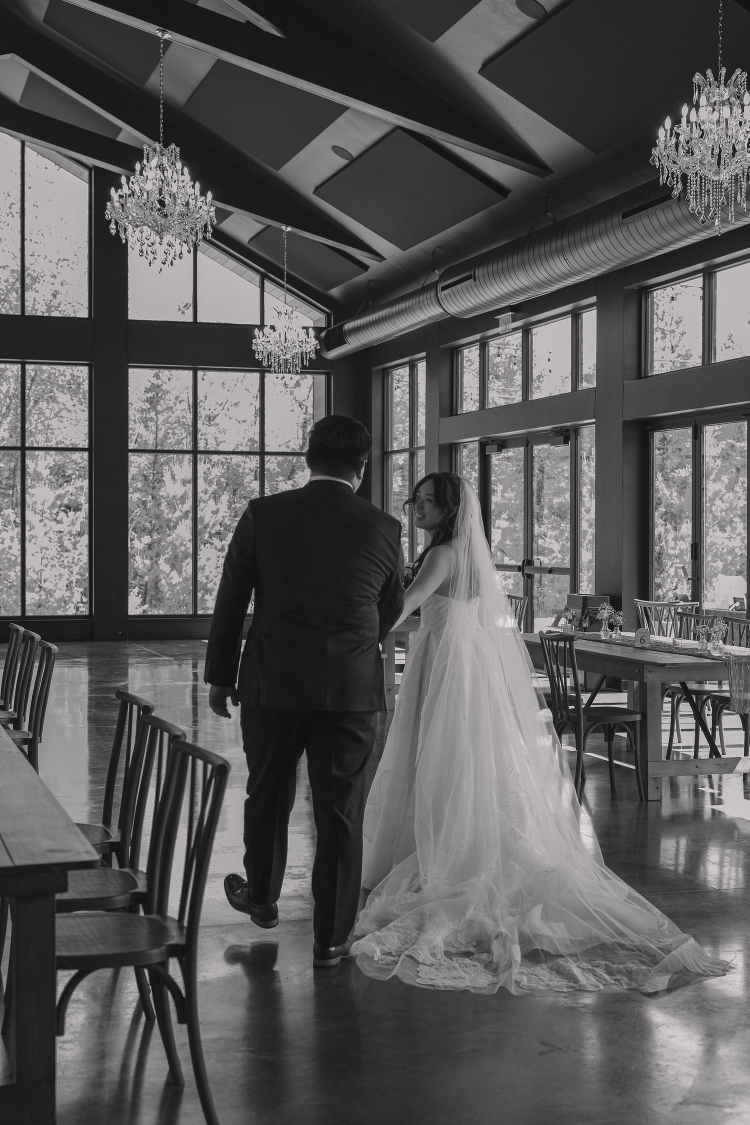 Black and white photo of bride and groom walking hand in hand through an elegant reception hall.