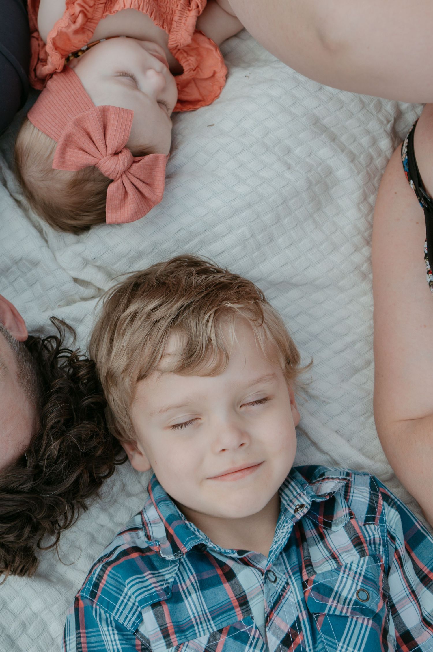 Older sibling lying beside newborn baby with a bow, Cochrane sibling portrait