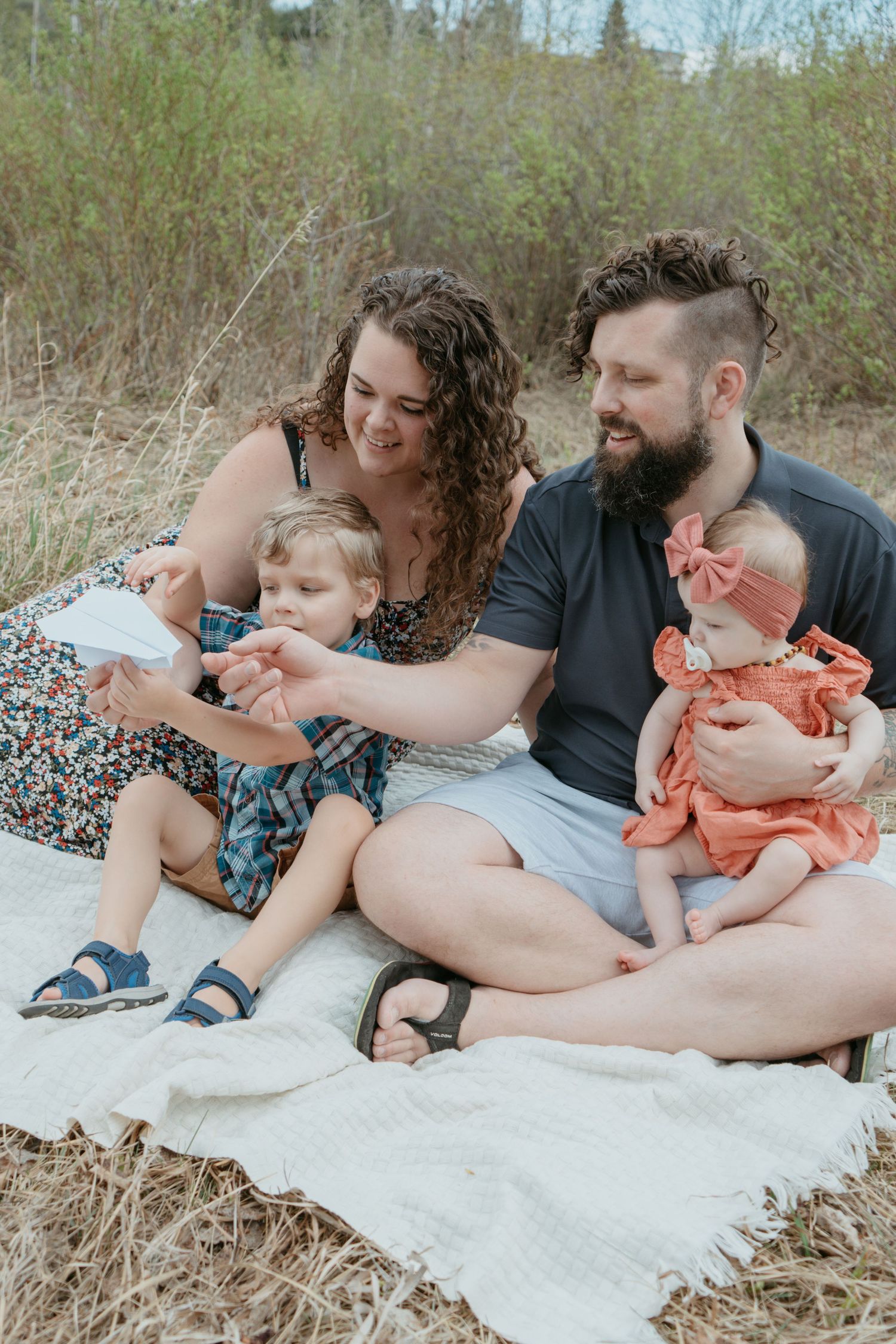 Family of four sitting together on a blanket in the Alberta foothills, Maddock Studios