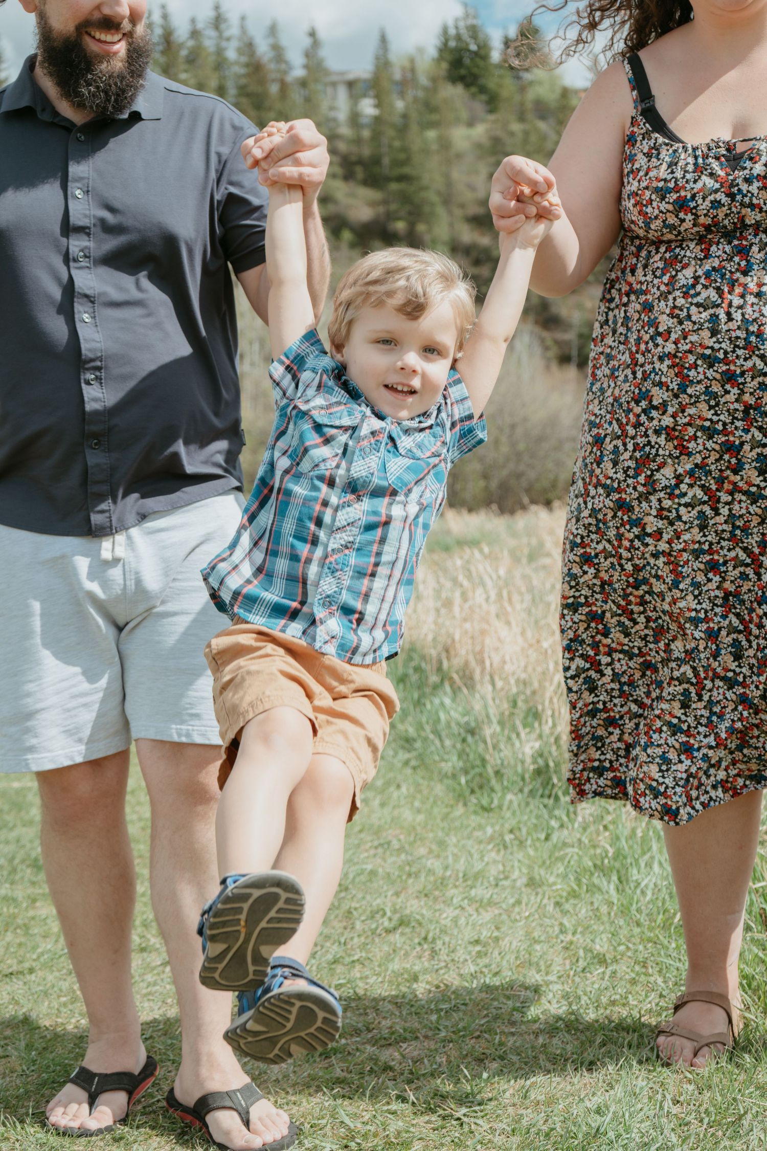 Parents swinging toddler between them in an open field, playful Alberta family photography