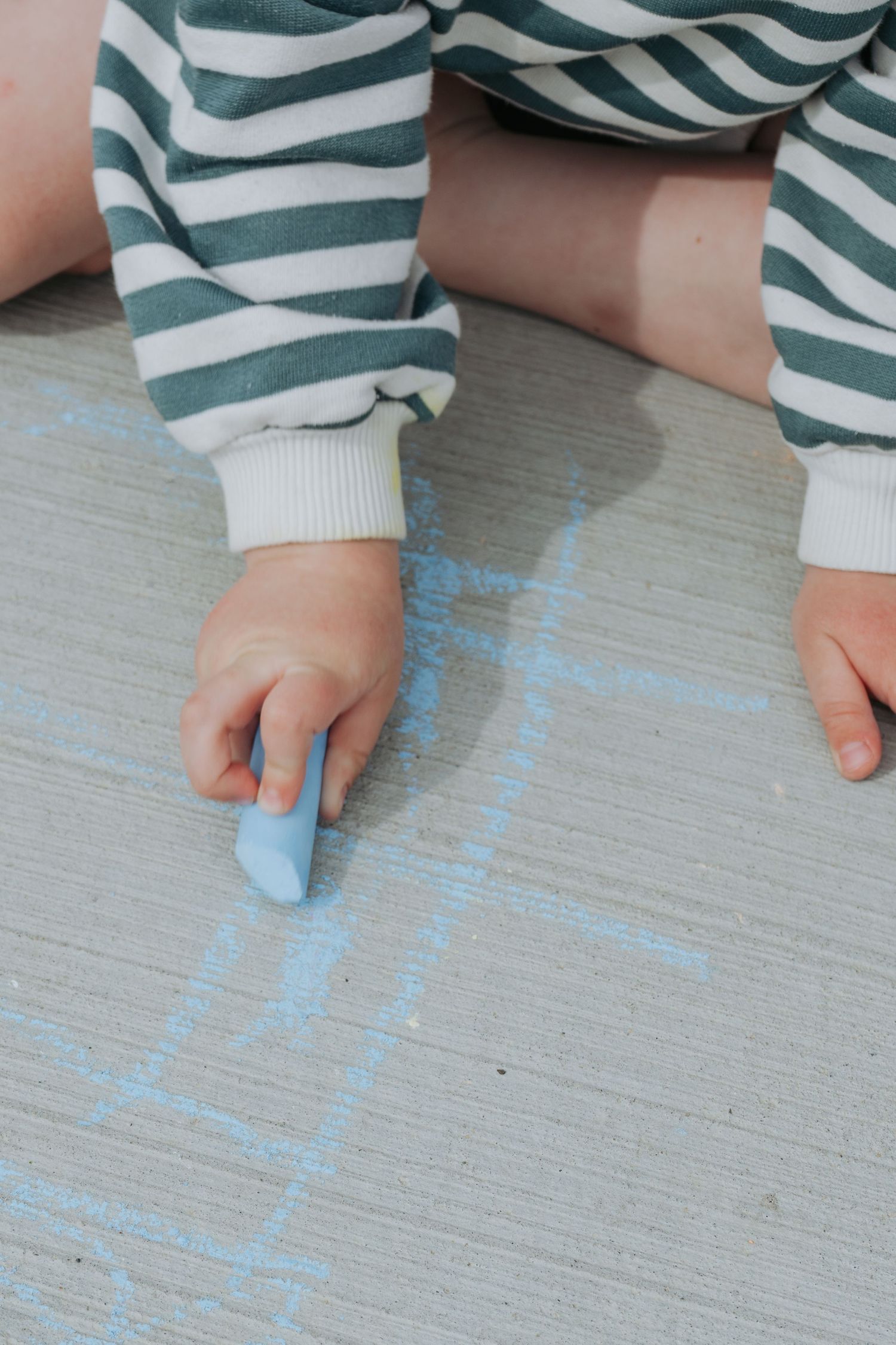 Toddler drawing with chalk on the ground, candid childhood moment captured by Maddock Studios