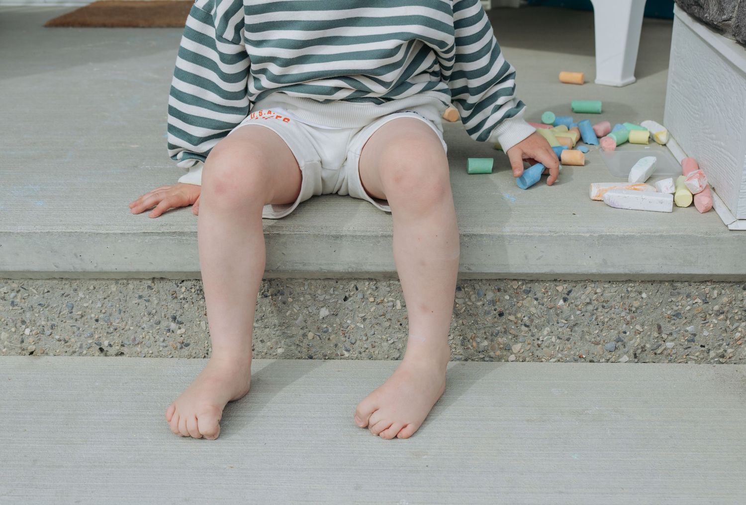 Toddler sitting on a step barefoot with small toys, candid childhood moment