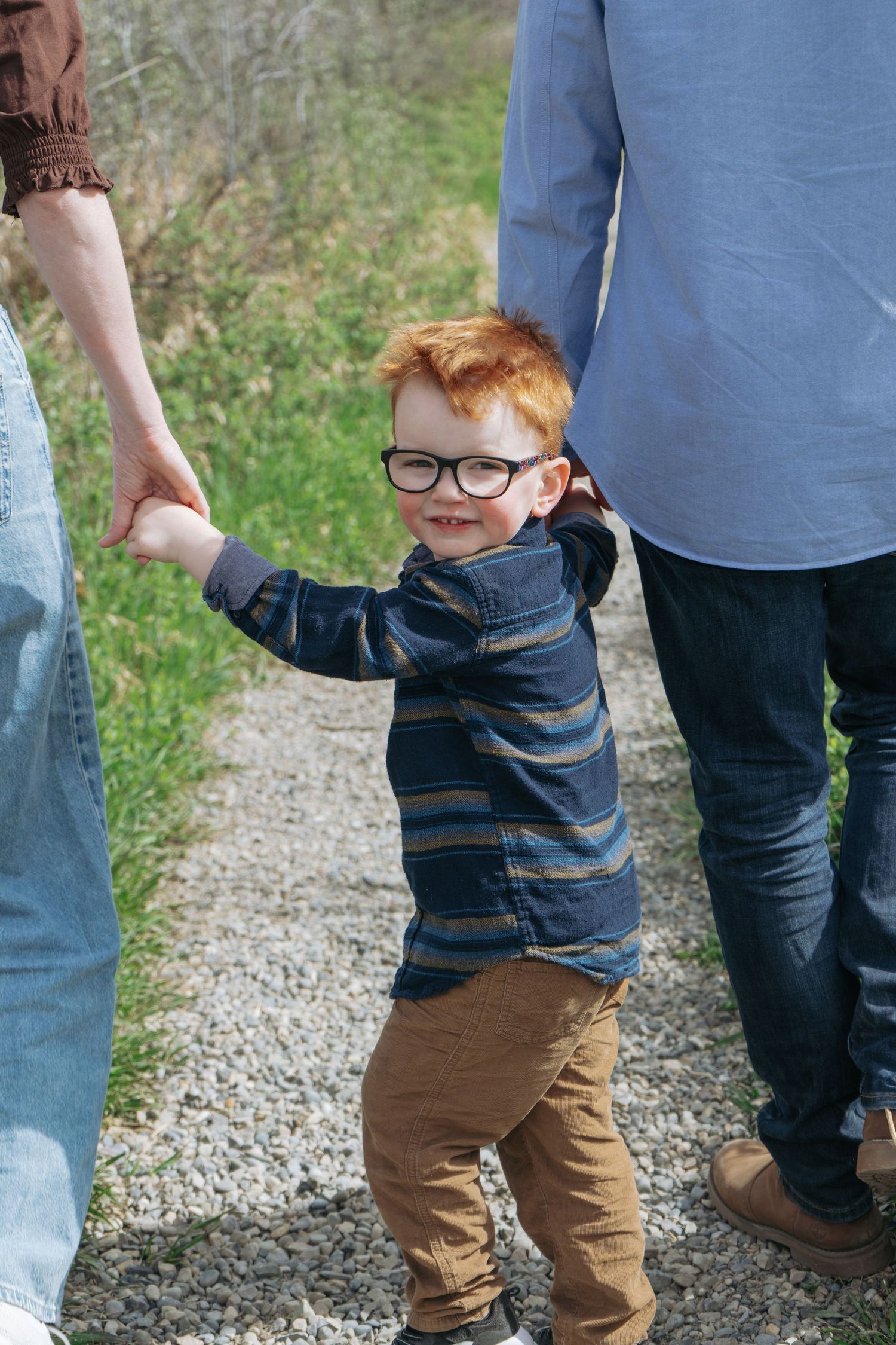 Red-haired toddler walking on a gravel path holding a parent's hand, Cochrane family portrait