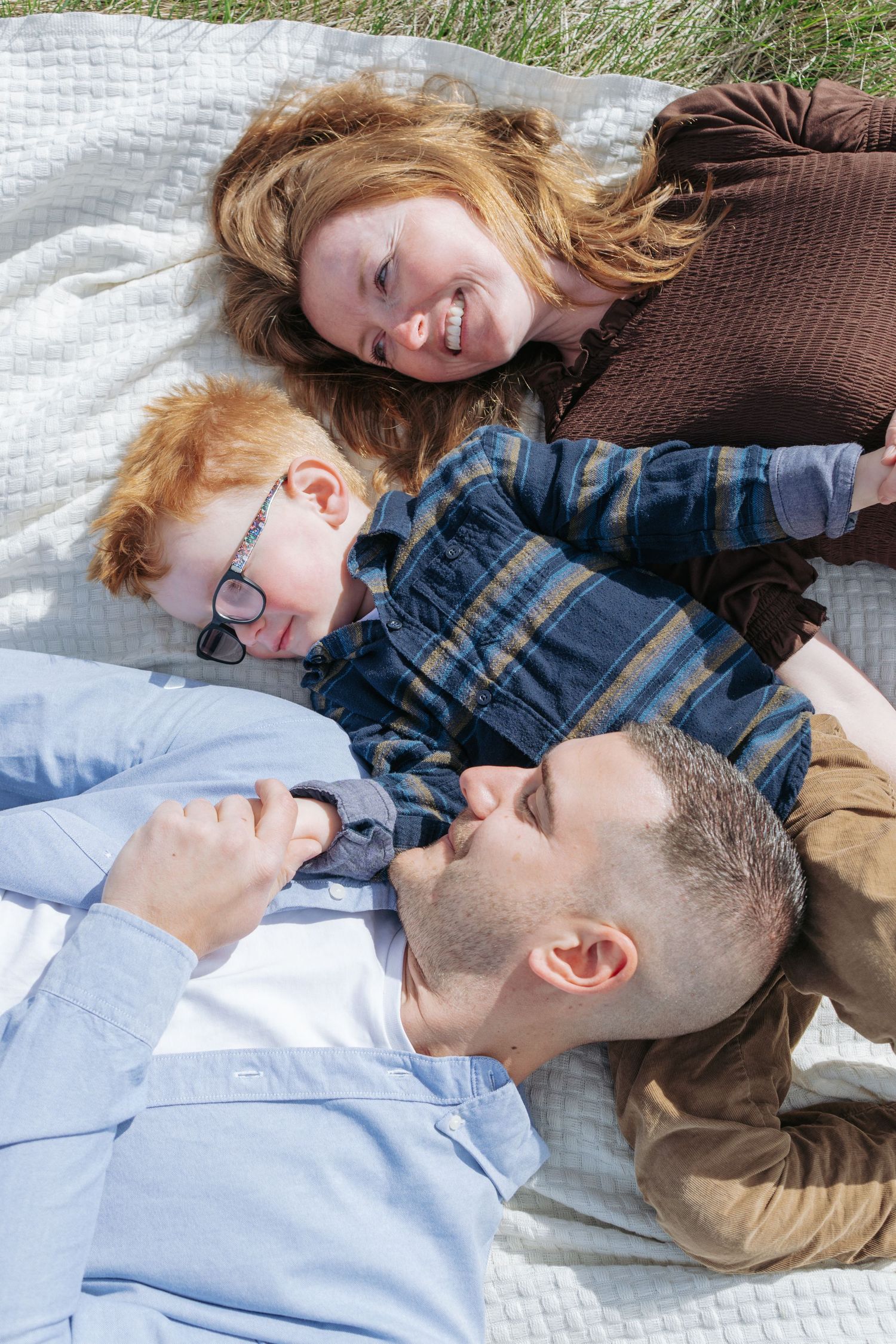 Family of three lying on a blanket looking up at the camera, candid Alberta family portrait
