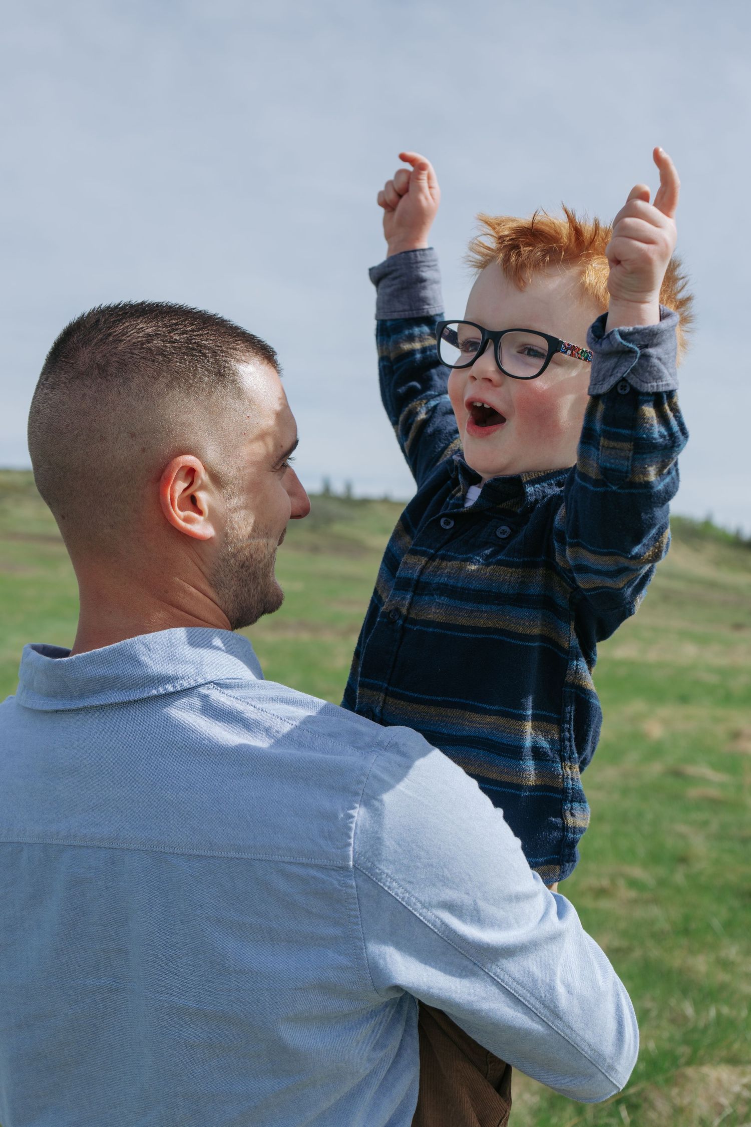 Dad holding red-haired toddler up in the air outdoors, joyful Cochrane family portrait