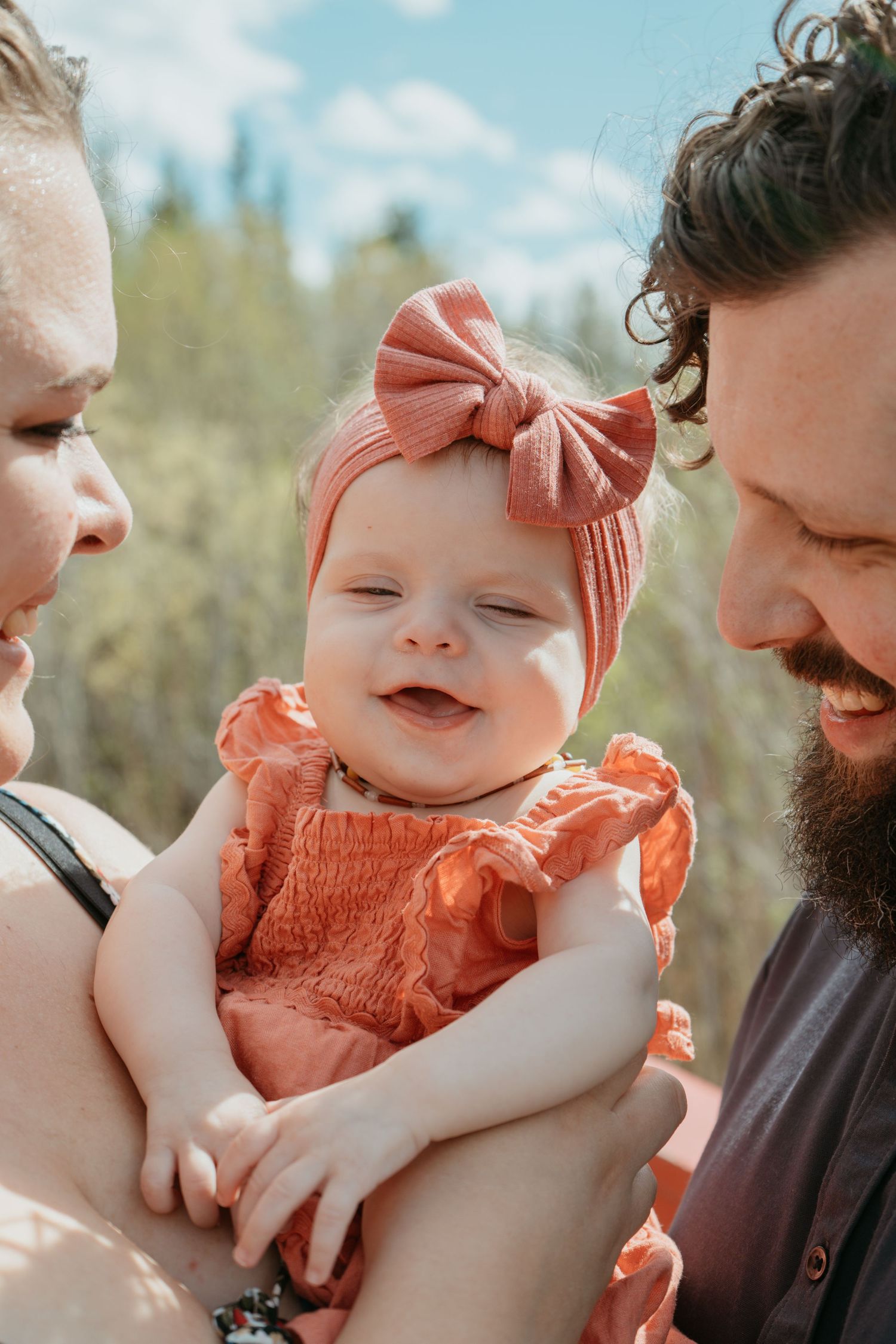 Parents cradling smiling baby girl in orange outfit, Cochrane newborn and family photography