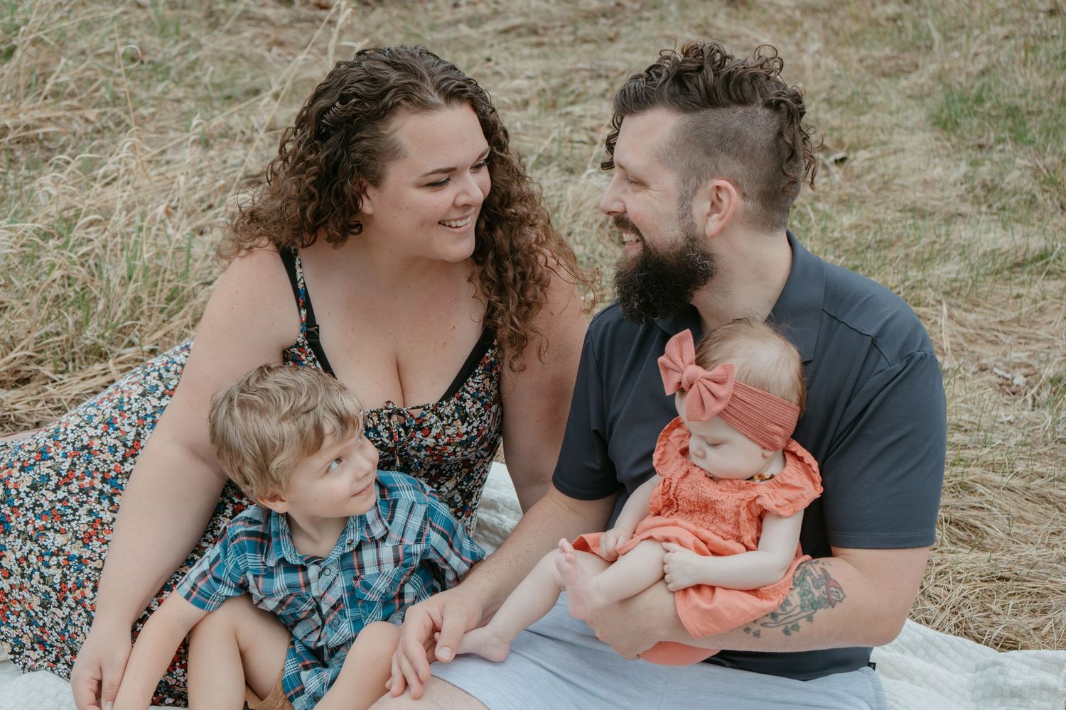 Family of four sitting together in a dry grass field, Alberta family portrait by Maddock Studios
