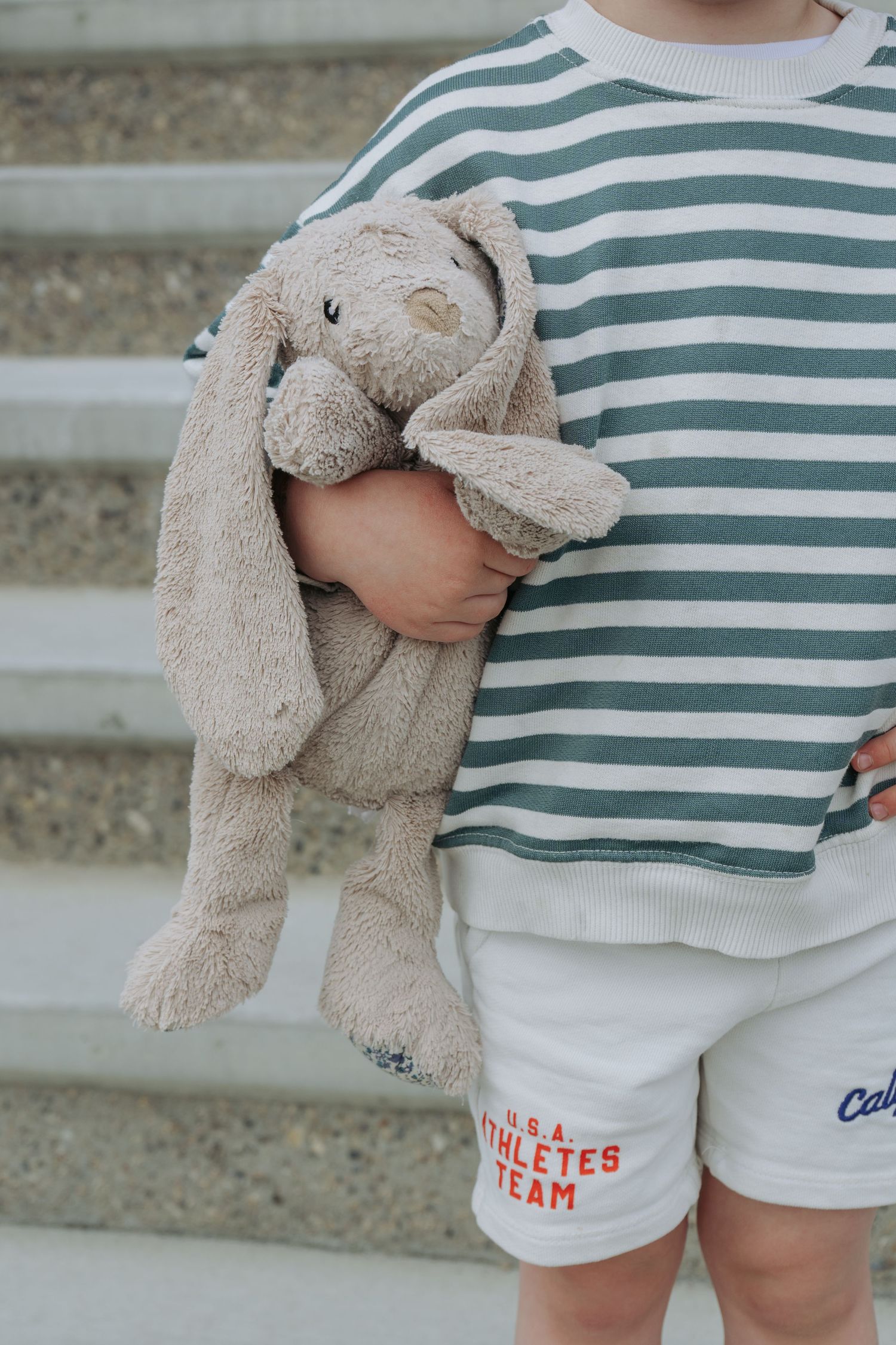 Young child holding a stuffed bunny toy on the front steps, sweet childhood detail shot