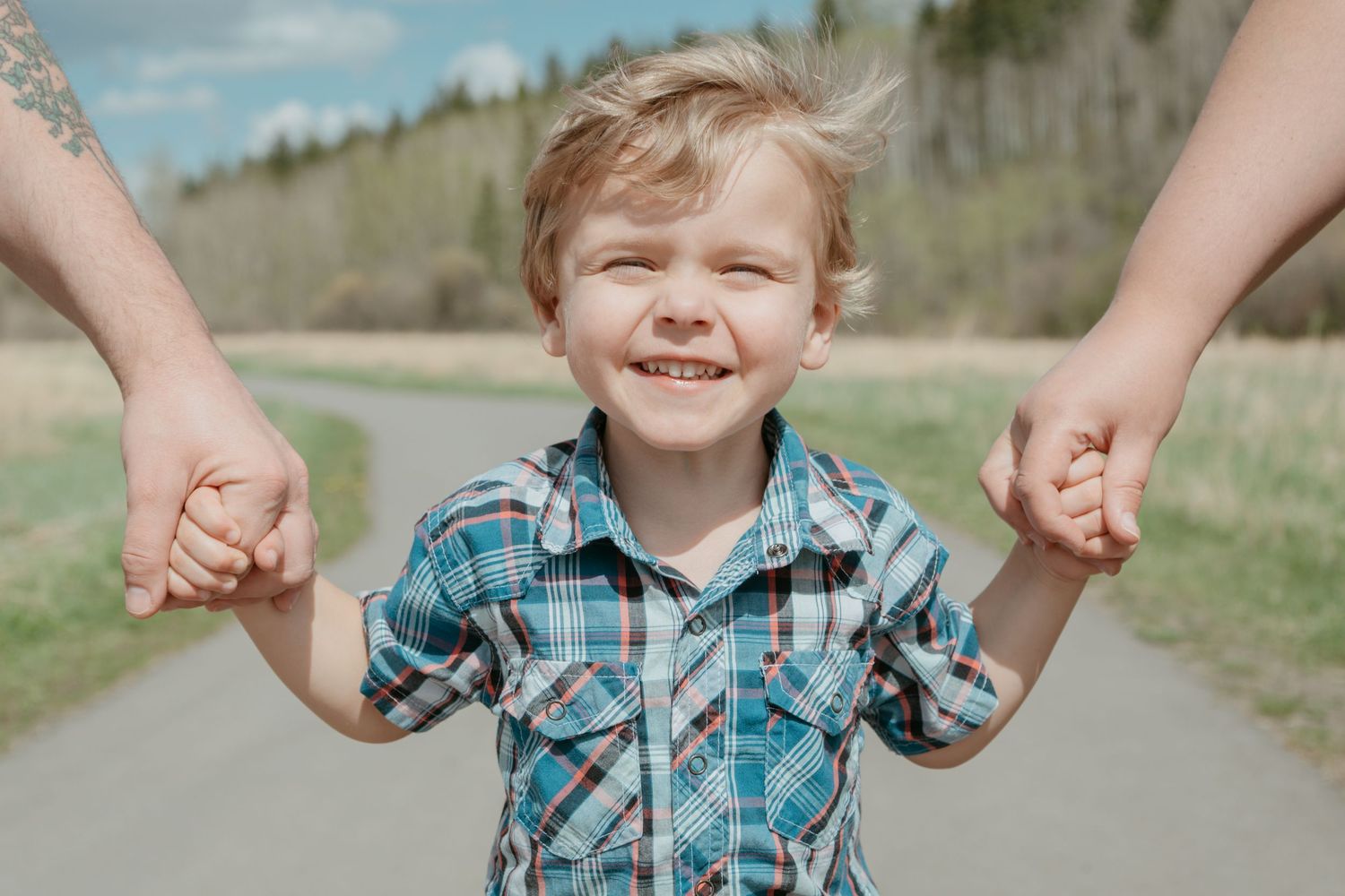 Happy toddler boy holding both parents' hands on a path, Bow Valley family portrait