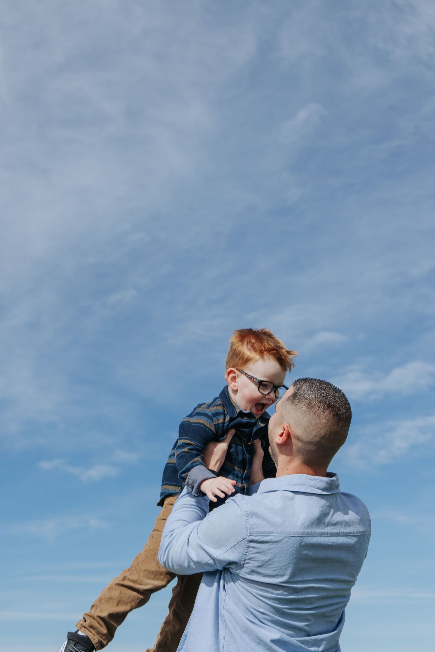 Dad lifting red-haired child up against a big blue sky, Cochrane family portrait