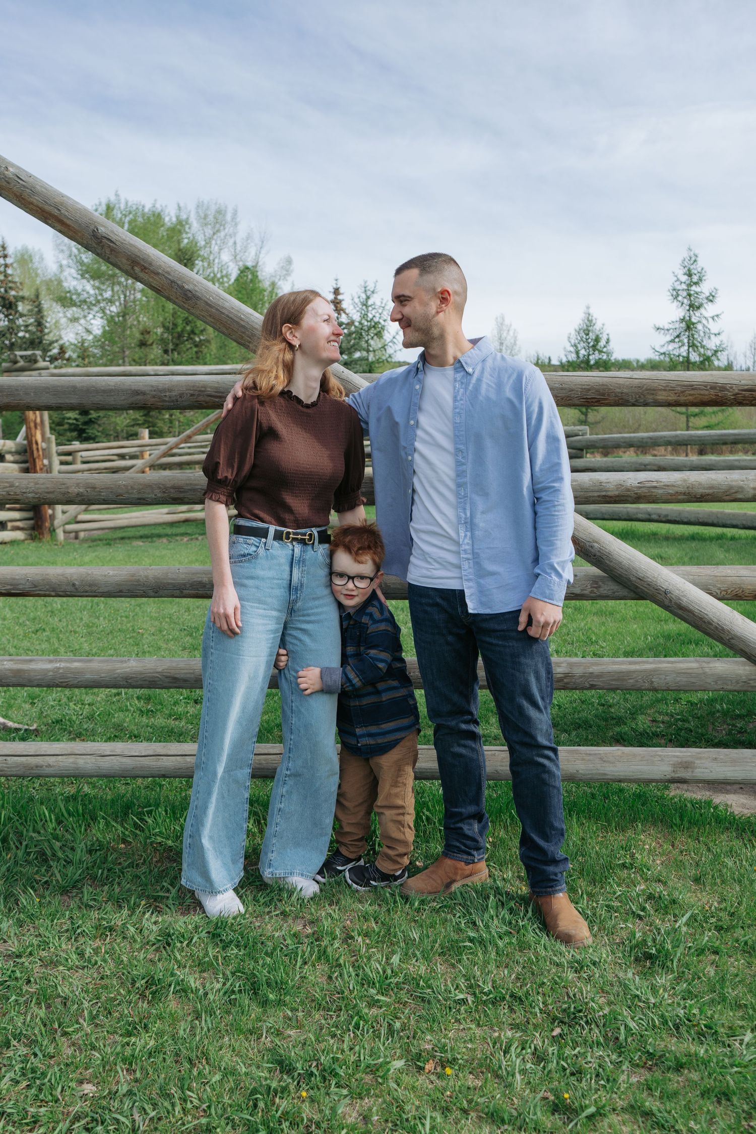 Family of three standing together by a wooden fence on an Alberta acreage, Maddock Studios