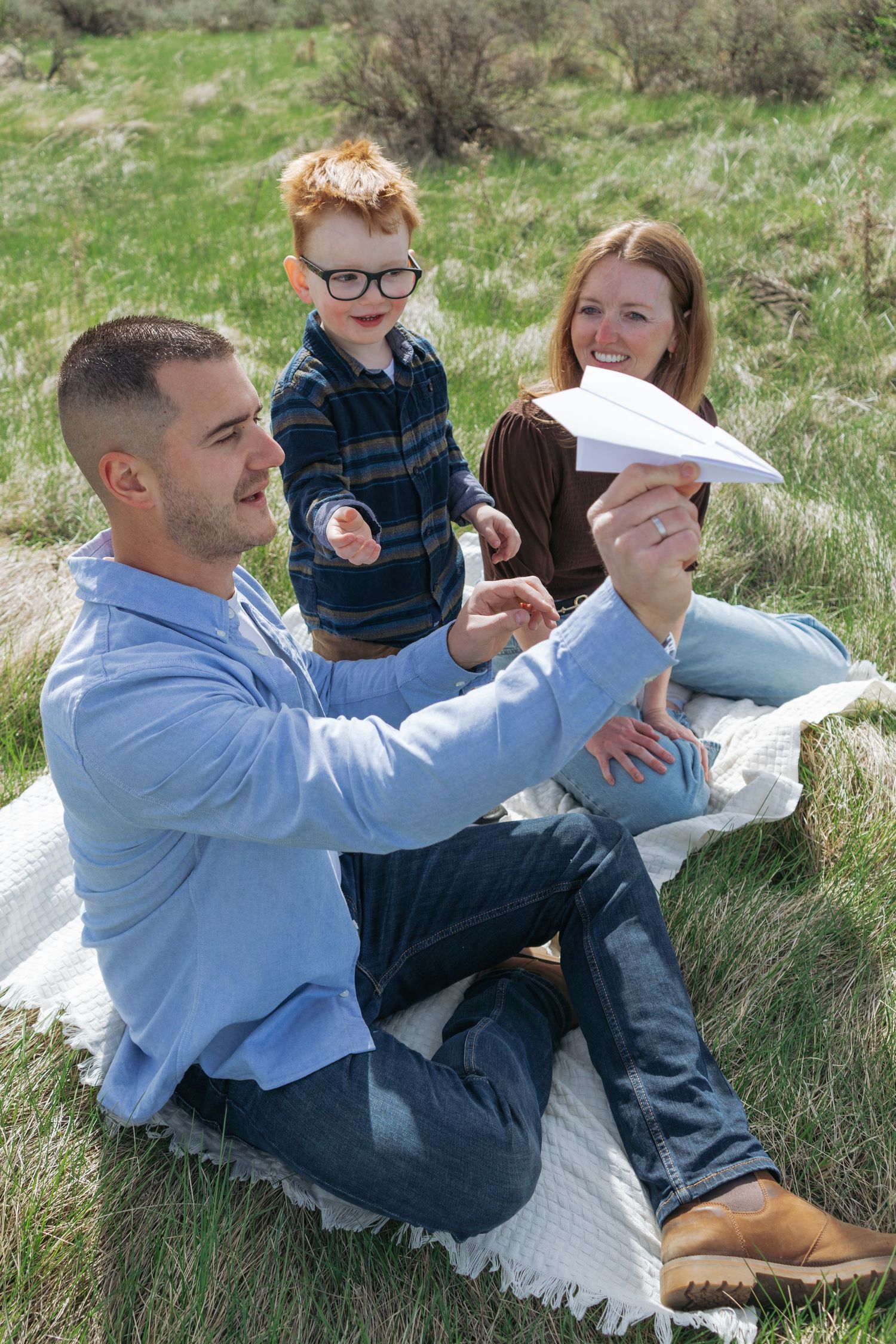 Family of four sitting together on a hillside, candid Alberta family portrait by Maddock Studios