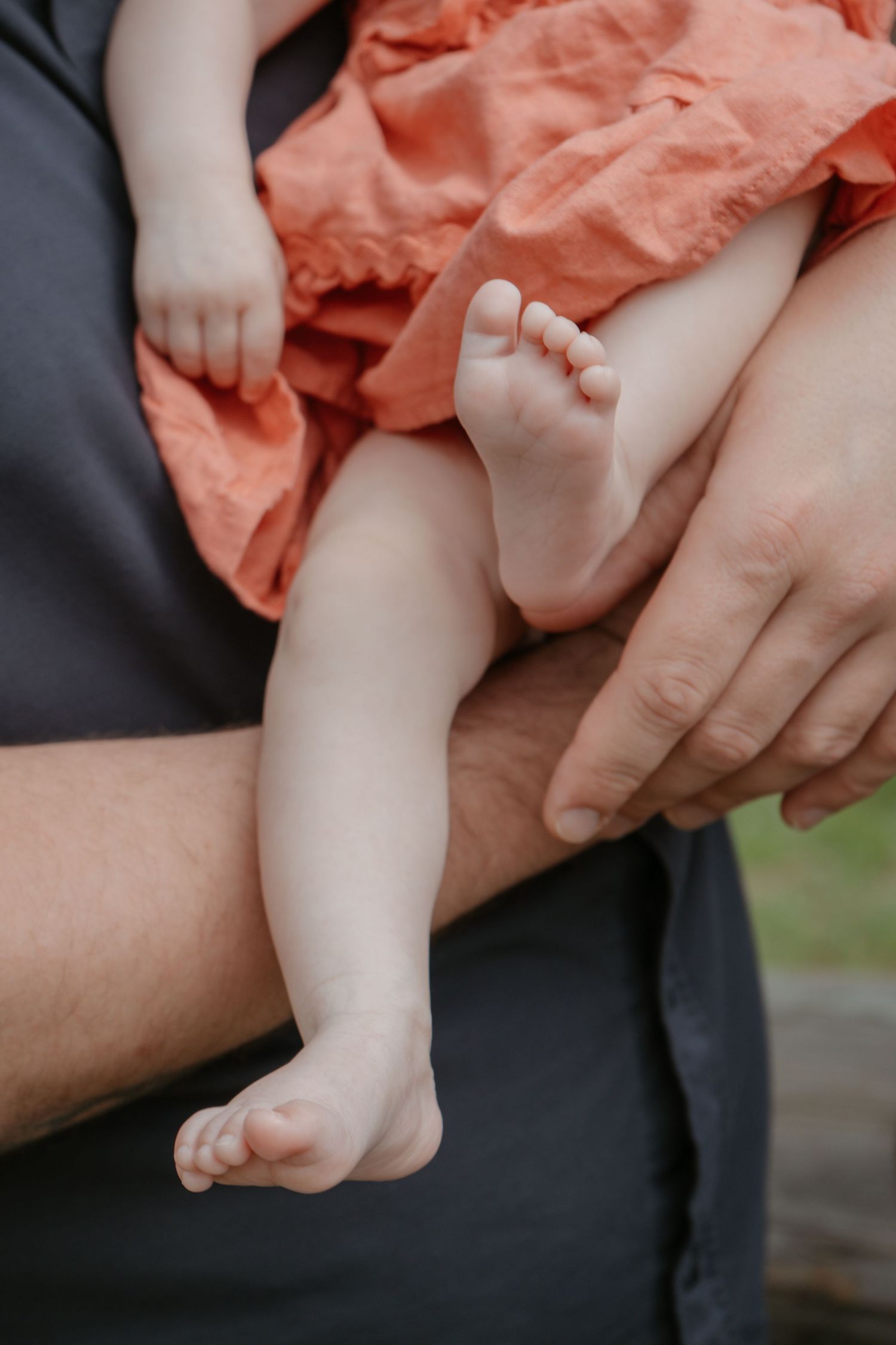Close-up of newborn baby feet in an orange outfit being held by a parent, Cochrane newborn photography