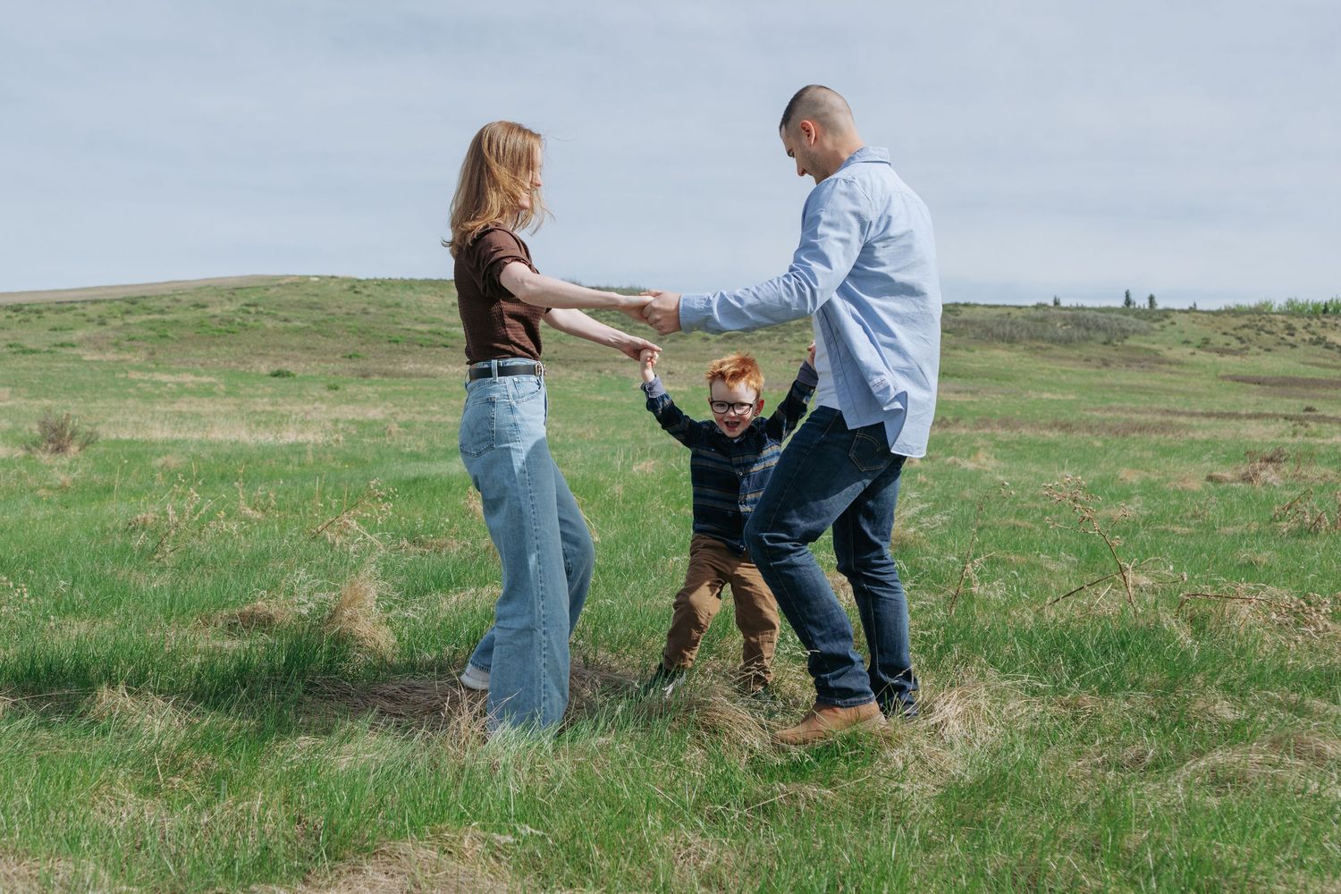 Family of three playing in open field, Alberta foothills family portrait by Maddock Studios