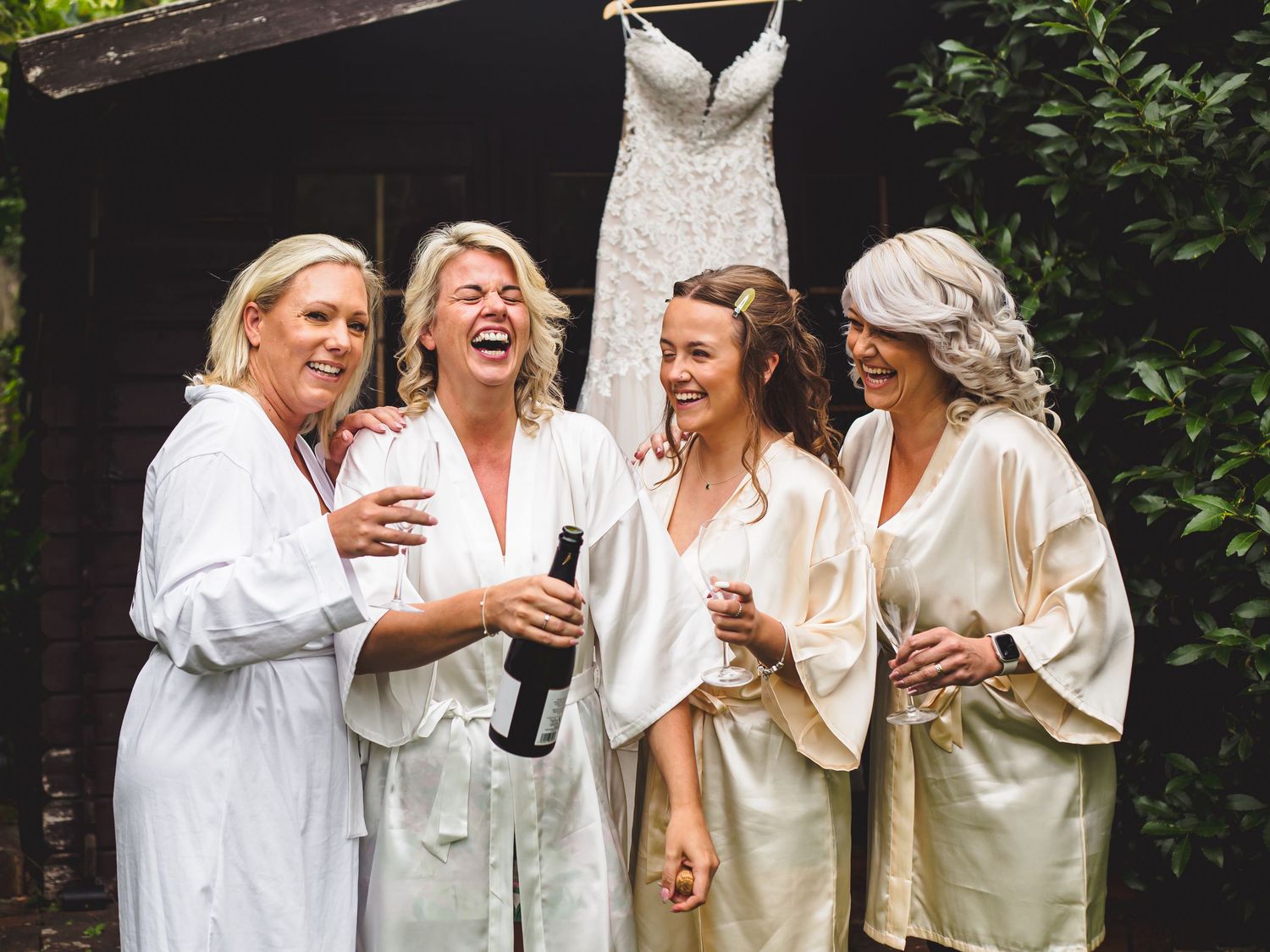 The Bridal party with matching robes enjoying a glass of champagne with the bride's wedding dress behind.