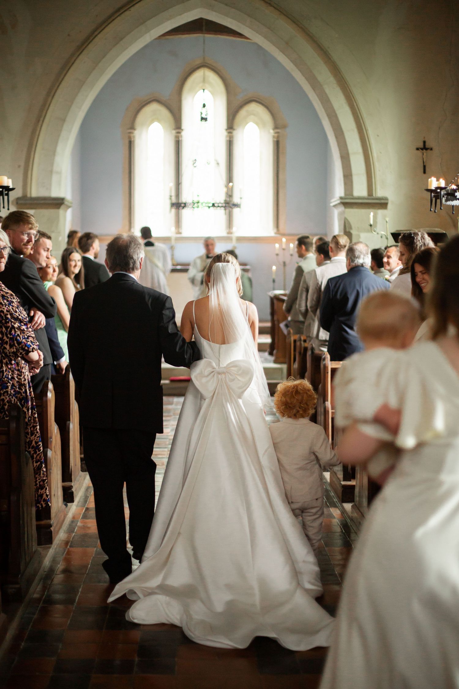 Wedding party walking down the aisle of a church with white arched ceilings and stained glass windows.