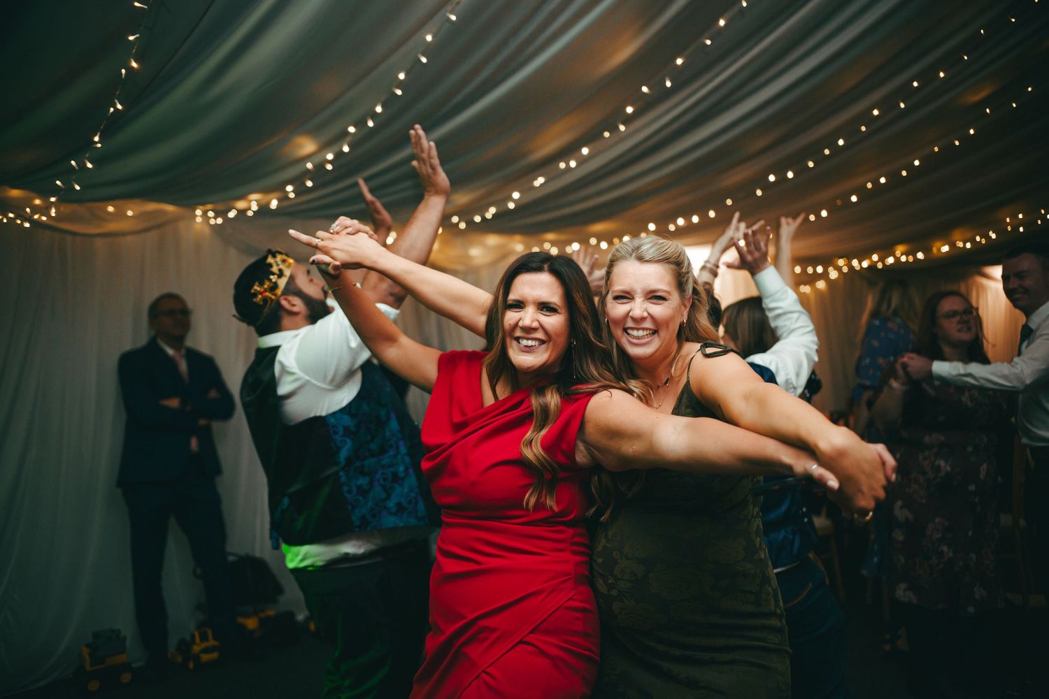 Wedding guests dance and celebrate together under twinkling string lights at an evening reception.