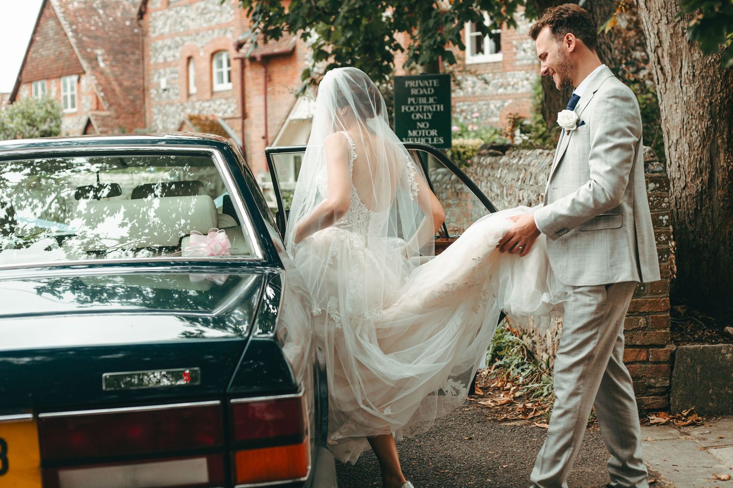 The groom helping his new wife into their wedding car in West Sussex