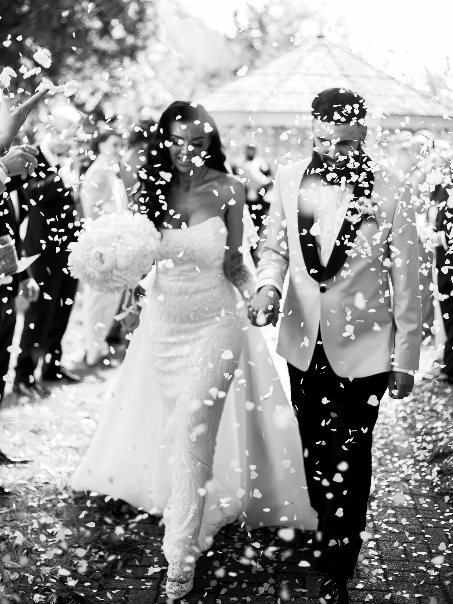 Wedding party celebrates with confetti and joy in black and white as they walk down a path together.