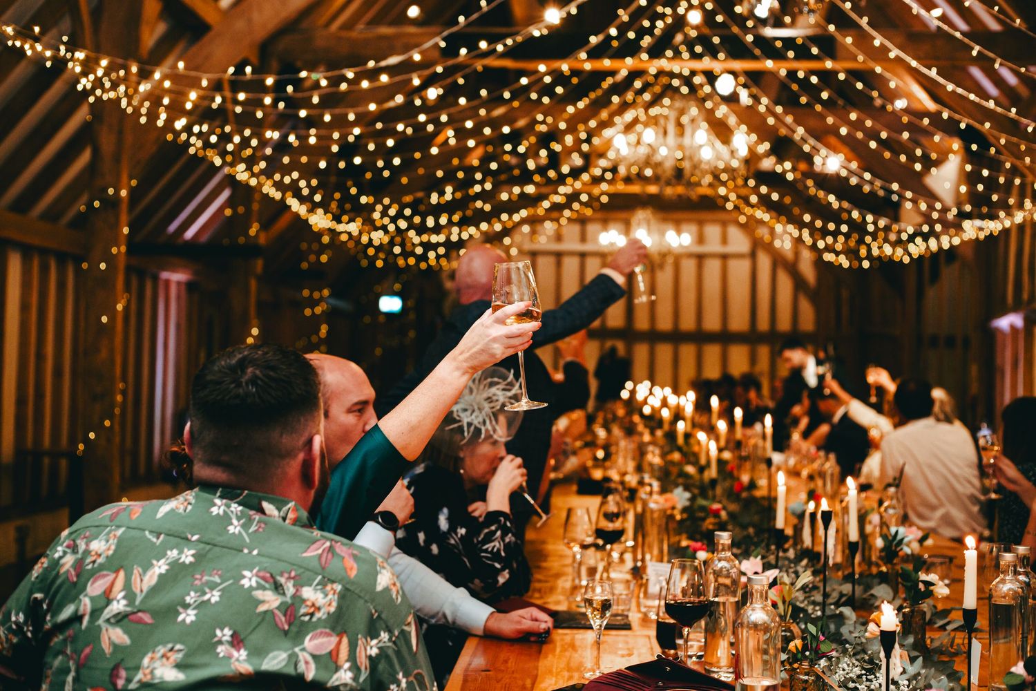 Wedding reception guests celebrate under warm string lights in the rustic wooden barn venue of Southend Barns, during evening festivities.