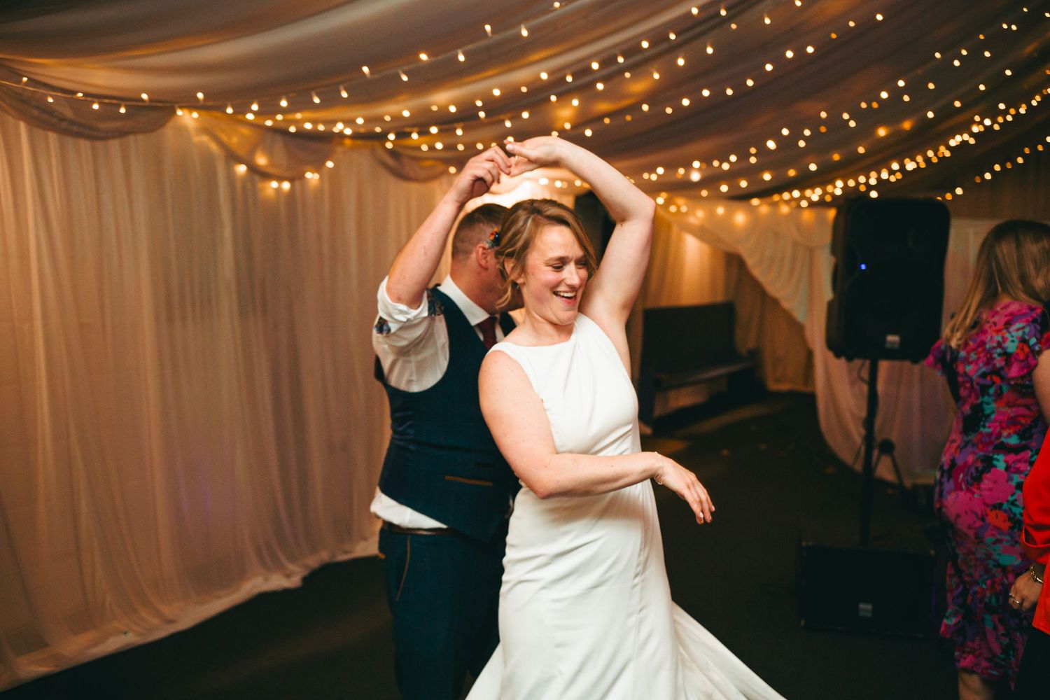 Wedding couple dances together under twinkling string lights at their reception celebration.