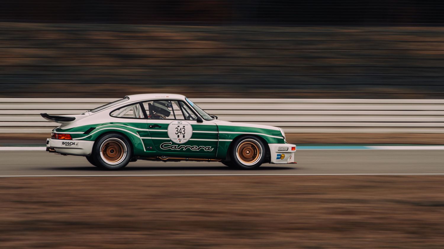 Vintage green Porsche 911 race car in motion on race track with panning shot effect.