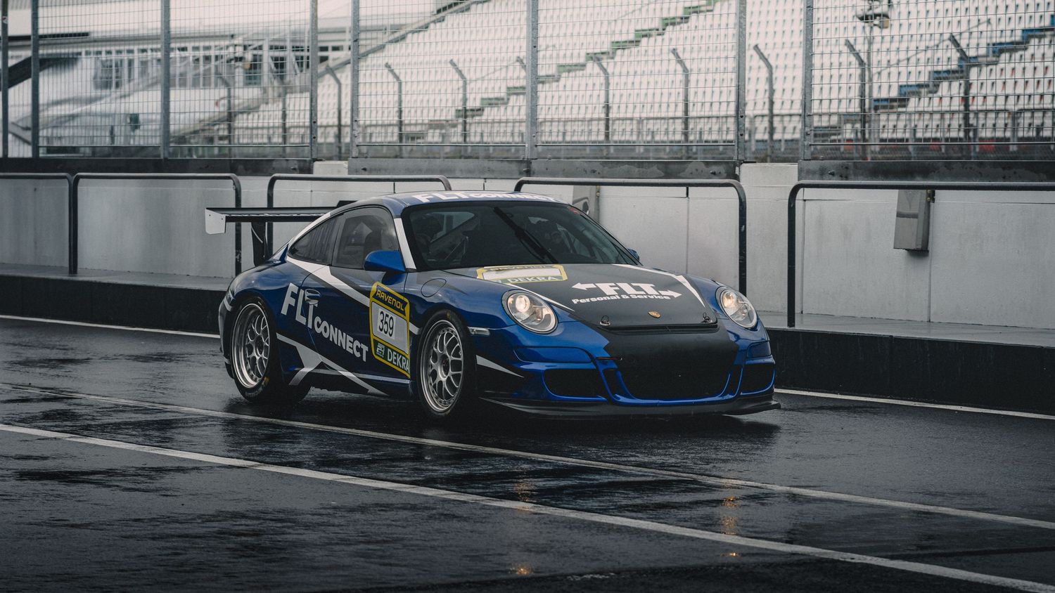 Blue Porsche race cars lined up along pit wall at a professional racing circuit.
