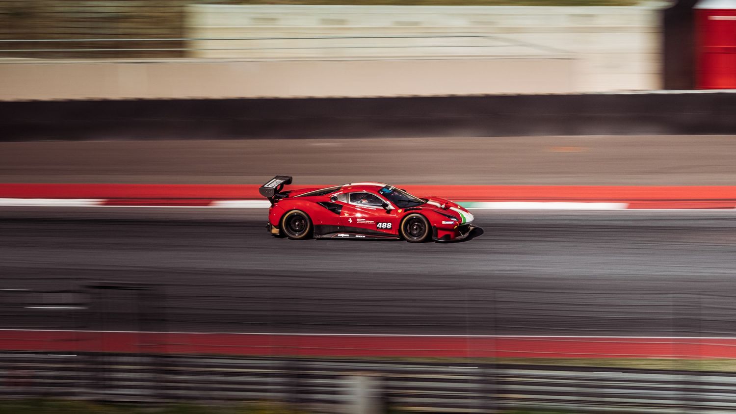 Red Ferrari race car speeding on track with motion blur background.