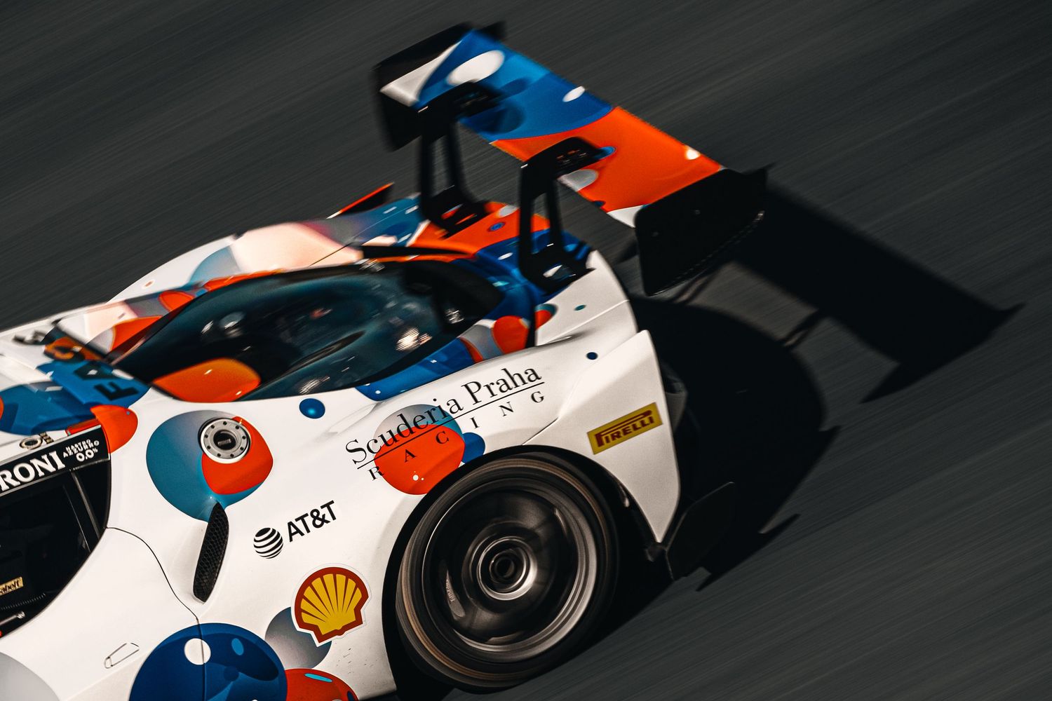 Colorful prototype race car with blue and orange livery speeding on a racetrack.