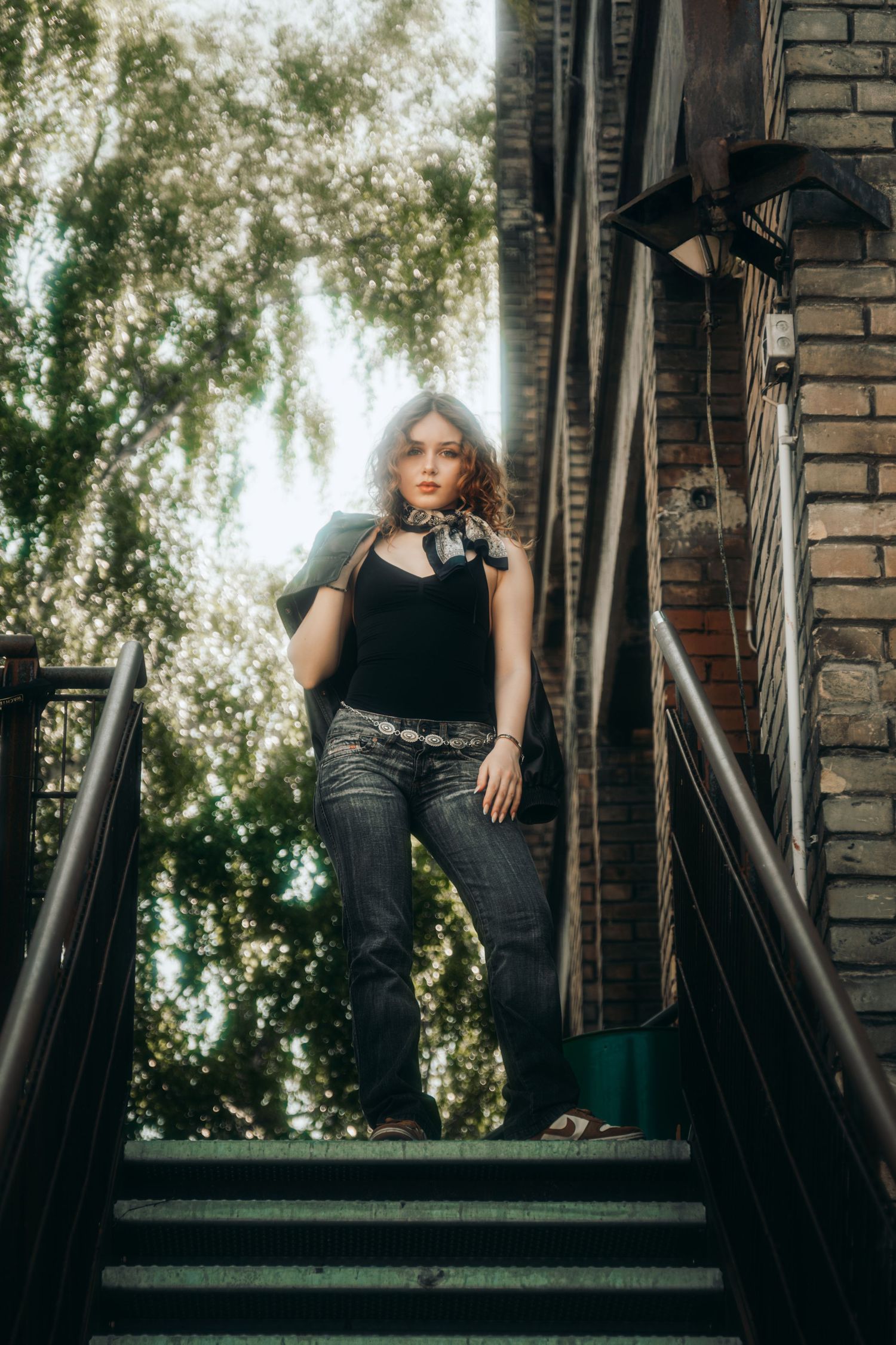 A person in dark clothing poses on outdoor brick steps with trees in the background creating a moody atmosphere.