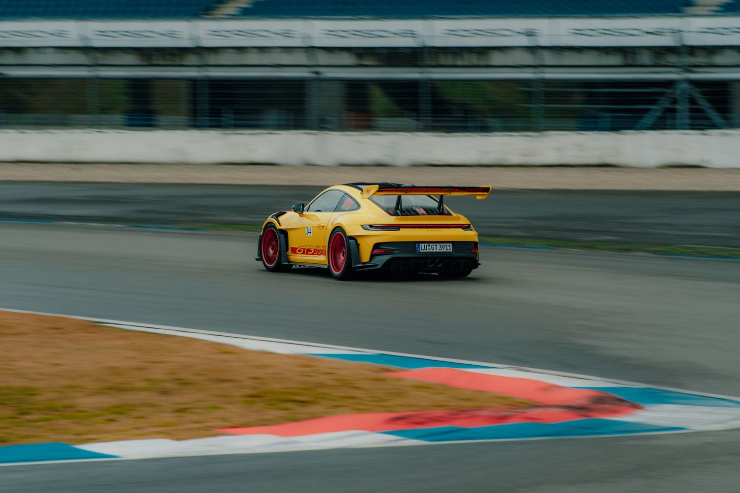 Yellow sports car racing on a track with distinctive red and blue curbing.