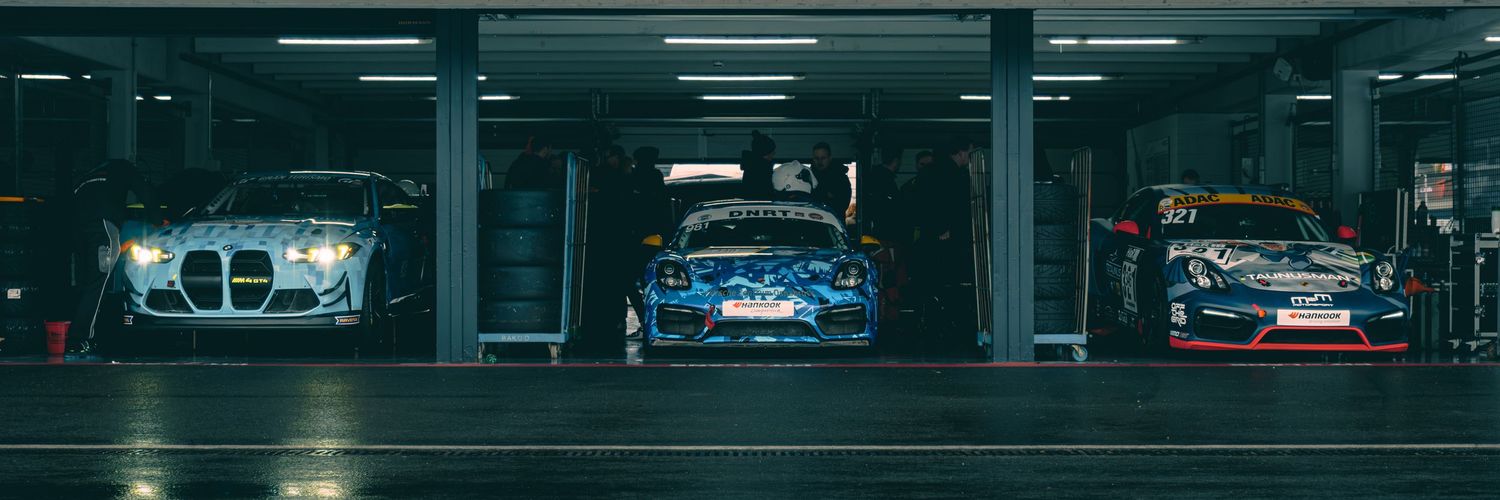 Dark garage interior showing multiple race cars parked in illuminated bays.