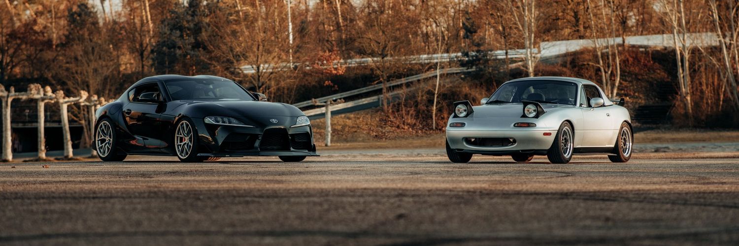 Sleek sports cars lined up at sunset with dramatic lighting and autumn trees in the background.