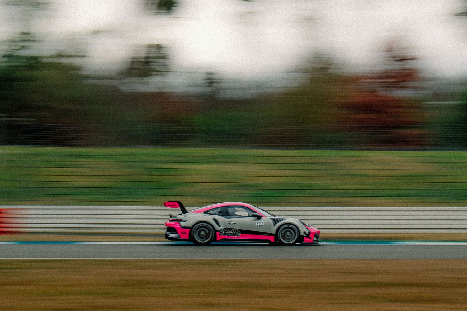 Pink Porsche GT3 race car speeding past on track with motion blur effect.