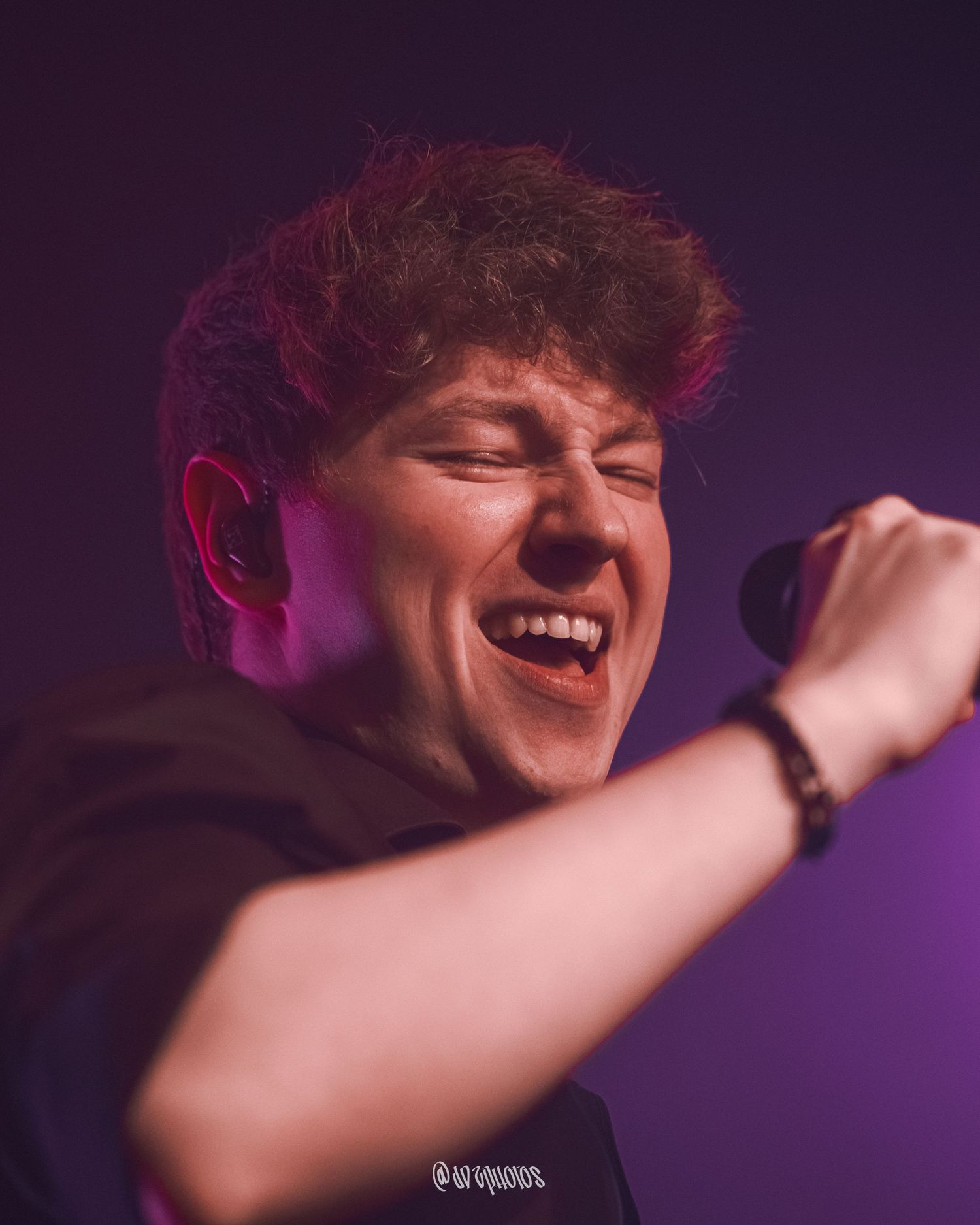 Concert performer singing passionately under purple stage lighting.