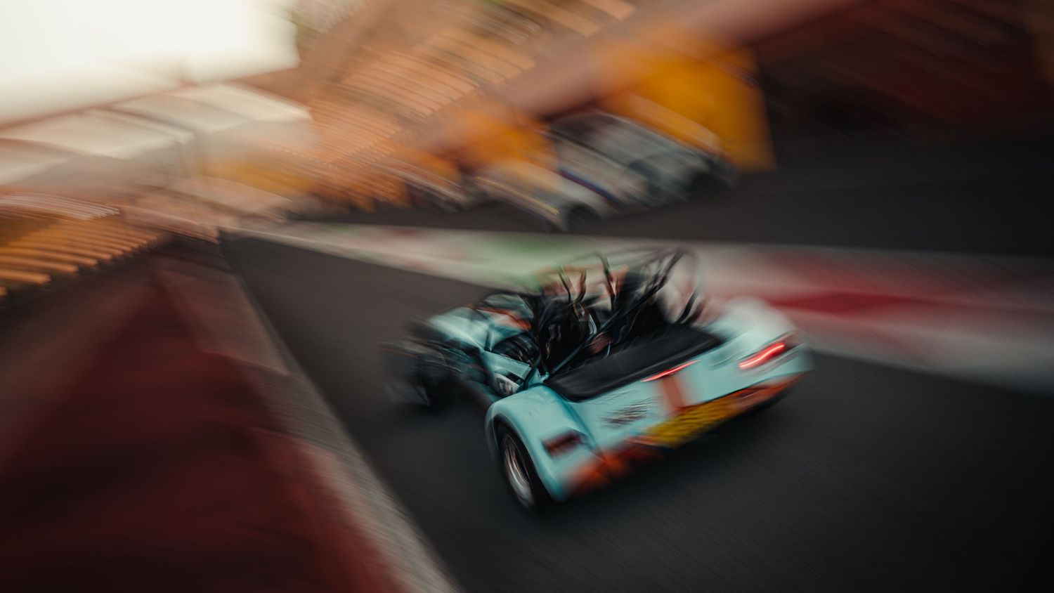 Vintage open-top Gulf-liveried racing car speeding through a circuit with dramatic motion blur effect.