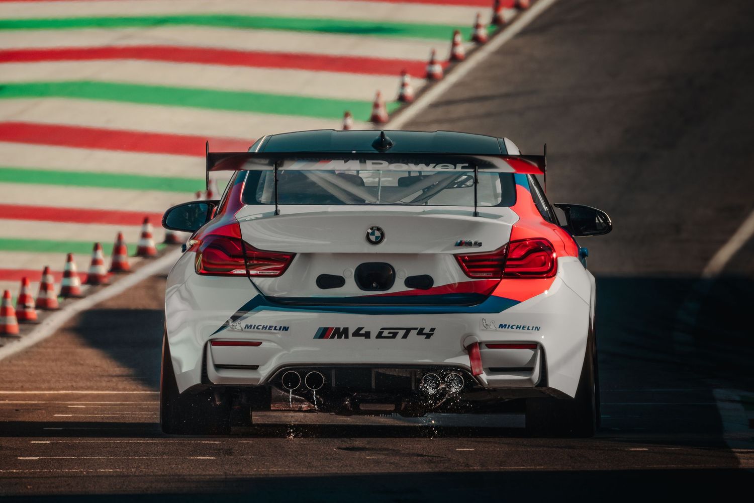 White BMW M4 GT4 race car seen from behind on a racing circuit track.