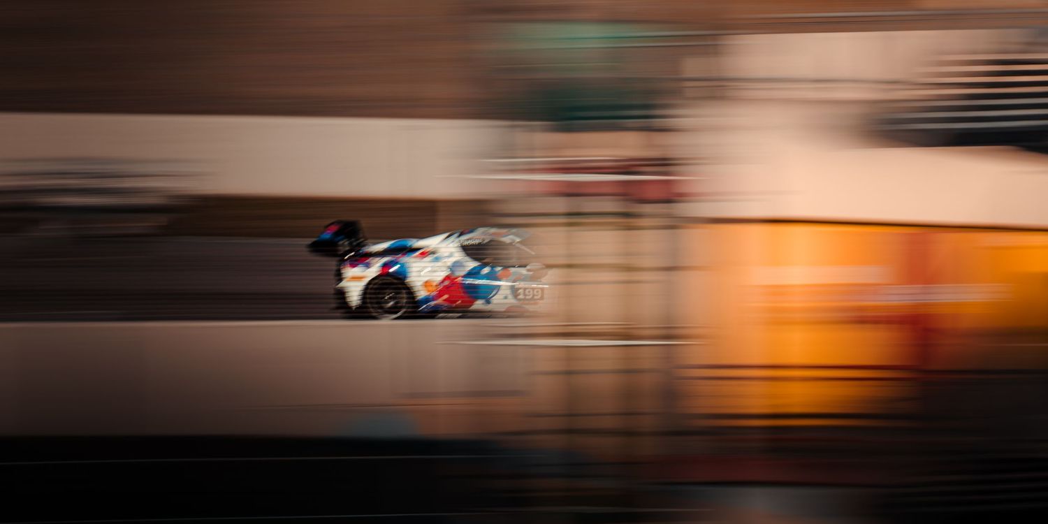 Colorful racing car captured in motion blur speeding along a race track at high speed.