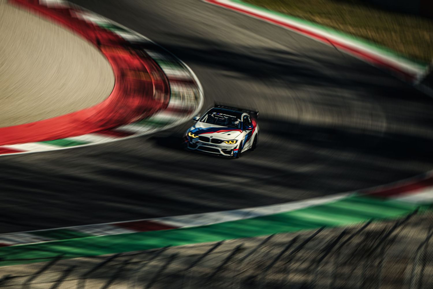 BMW M4 GT3 race car speeding through a curved track, captured with motion blur at a professional racing circuit.
