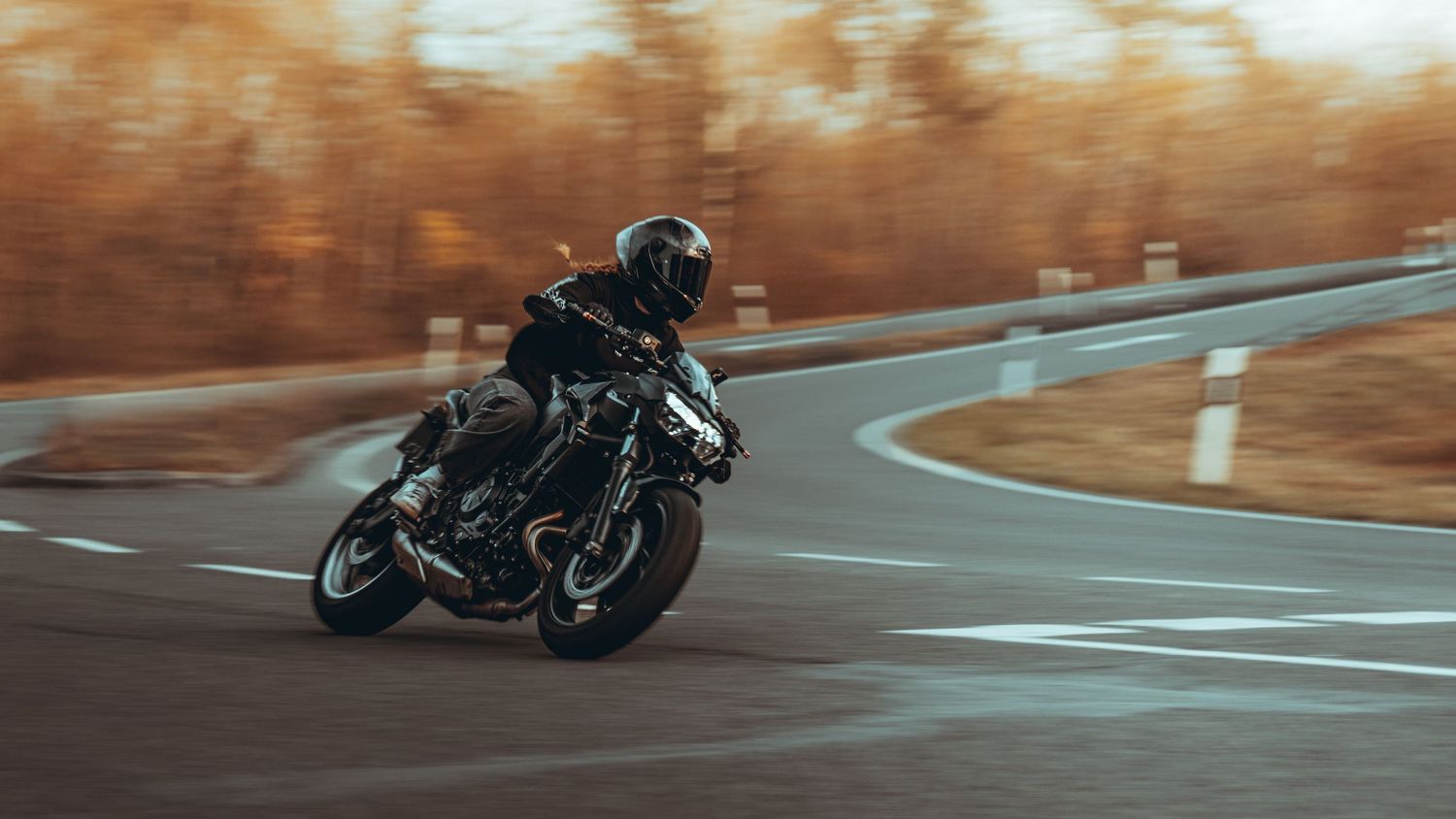 Motorcycle rider leaning into a sharp turn on an empty road surrounded by fall colors.