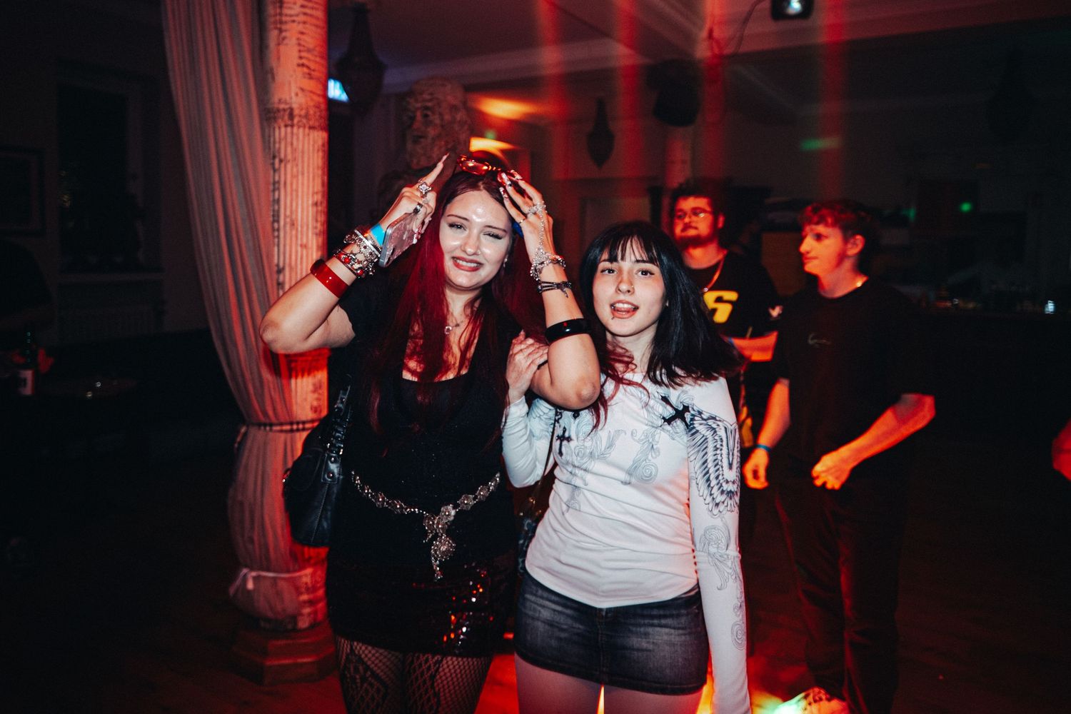 People dancing and enjoying themselves at a nightclub with red lighting and dark ambiance.