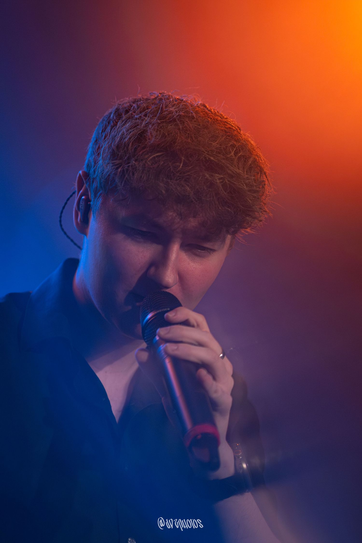 Close-up concert photo with dramatic orange and blue lighting gradient.